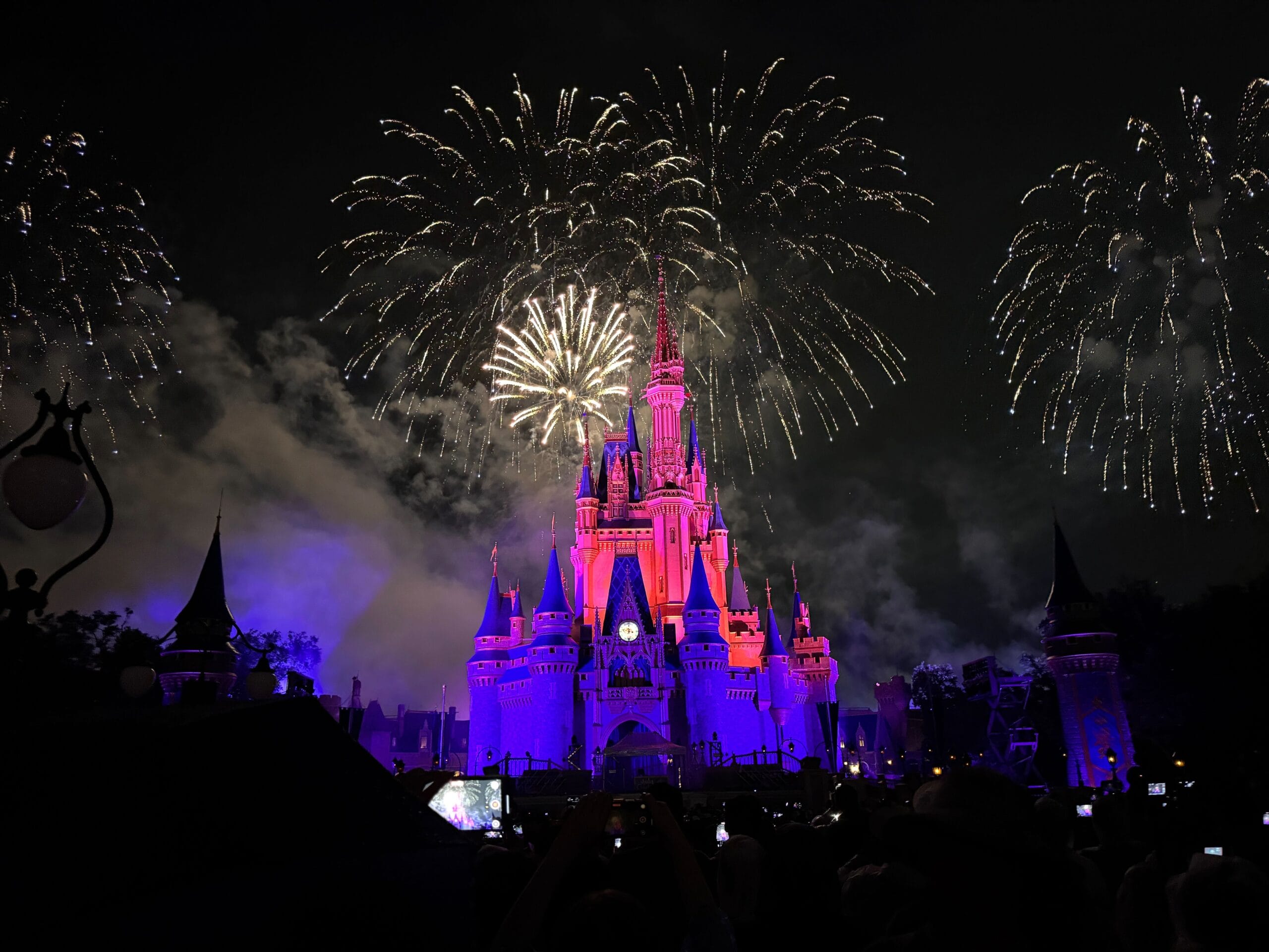 Disney castle lit in purple and pink at night with Fourth of July 2025 fireworks bursting as people celebrate America.
