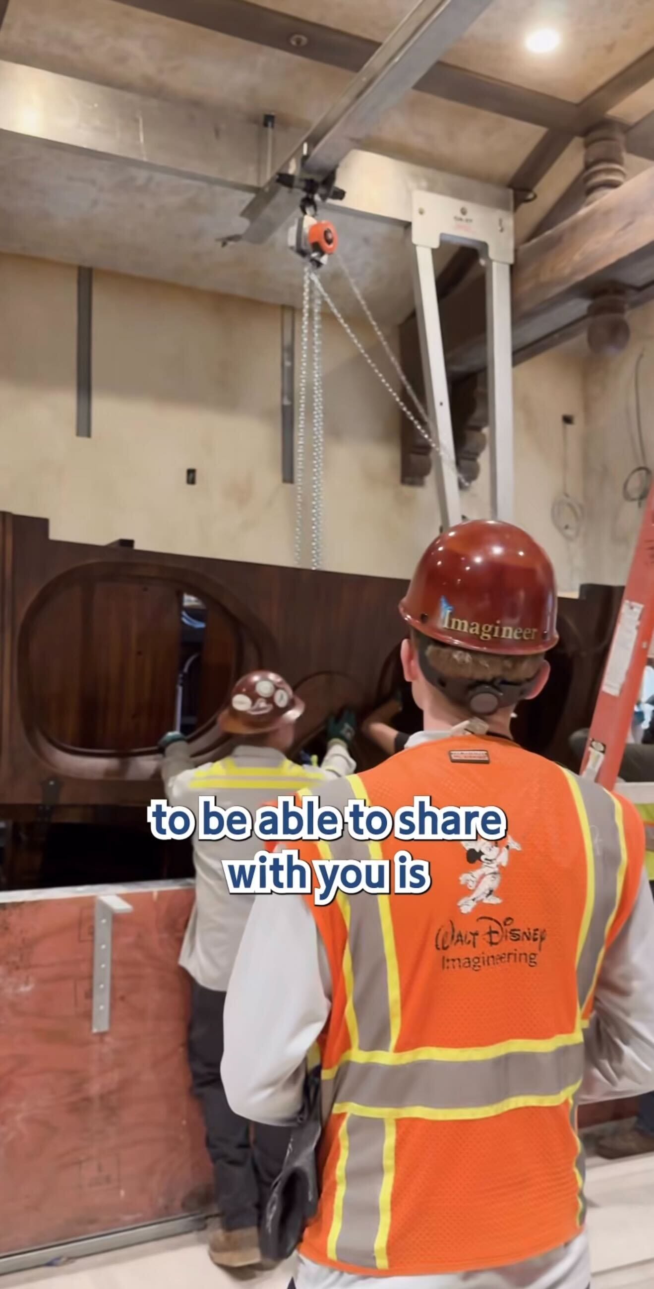Two workers in hard hats install a large wooden structure indoors for the Pirates Tavern at Magic Kingdom.