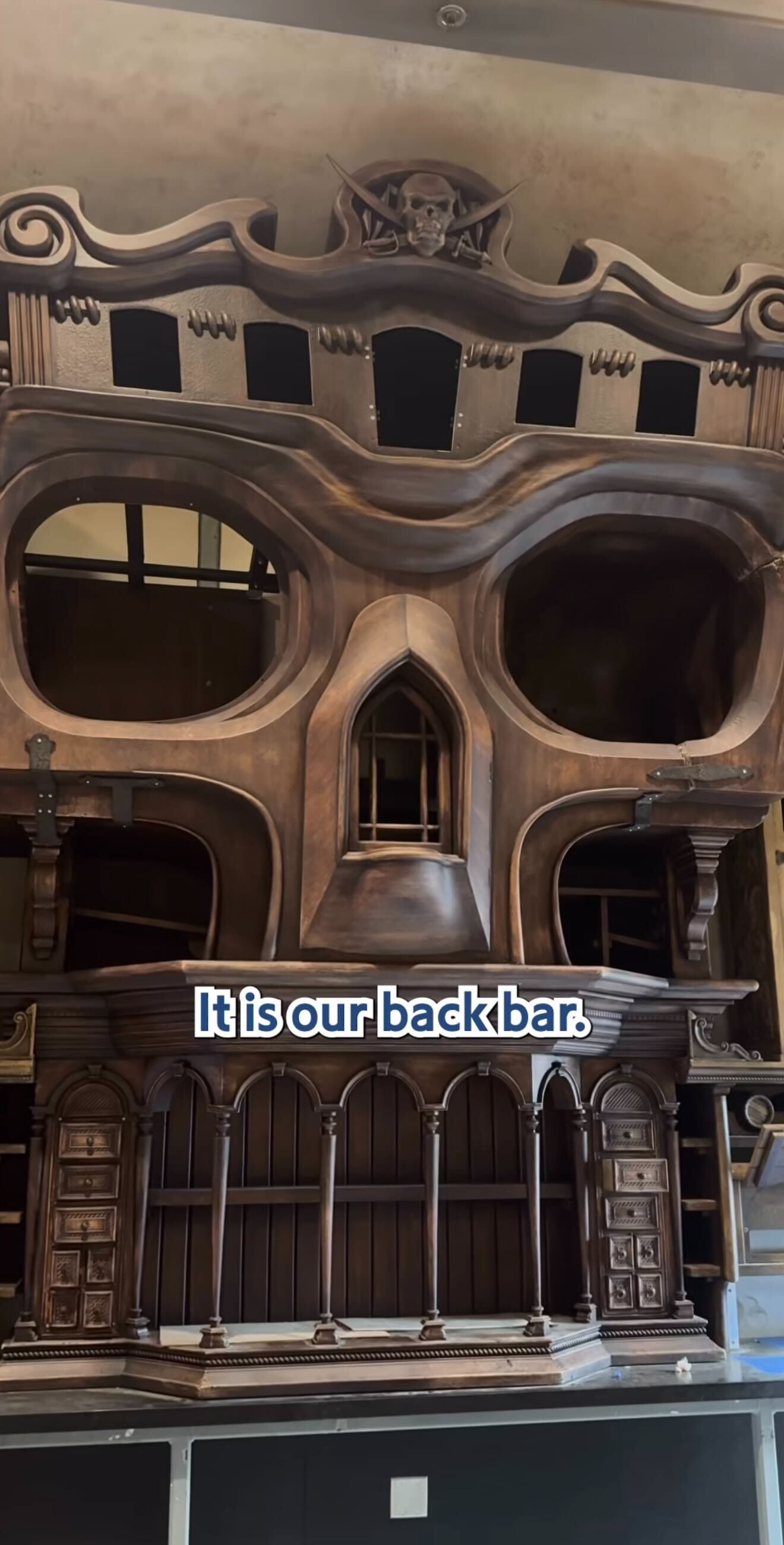 A large wooden backbar designed as a skull with shelves and cabinets, perfect for a pirates tavern. Text overlay: "It is our backbar.