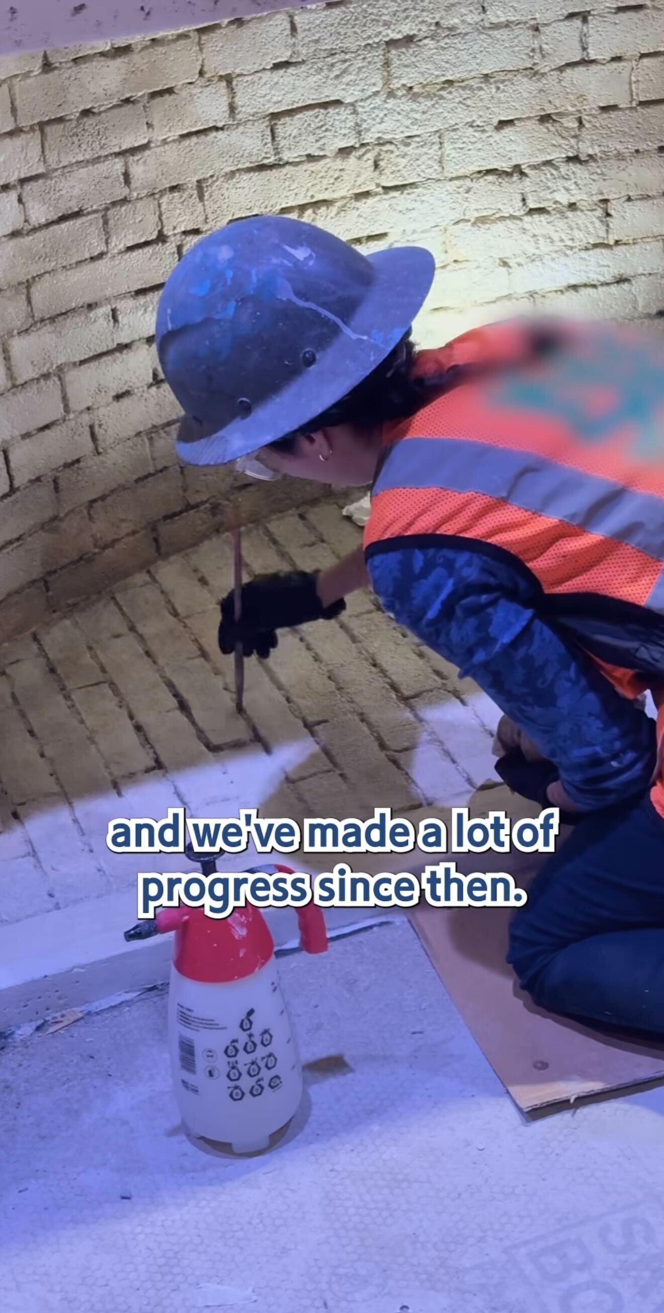 A construction worker in a hard hat builds a brick wall outside the Pirates Tavern, tools and spray bottle close by.