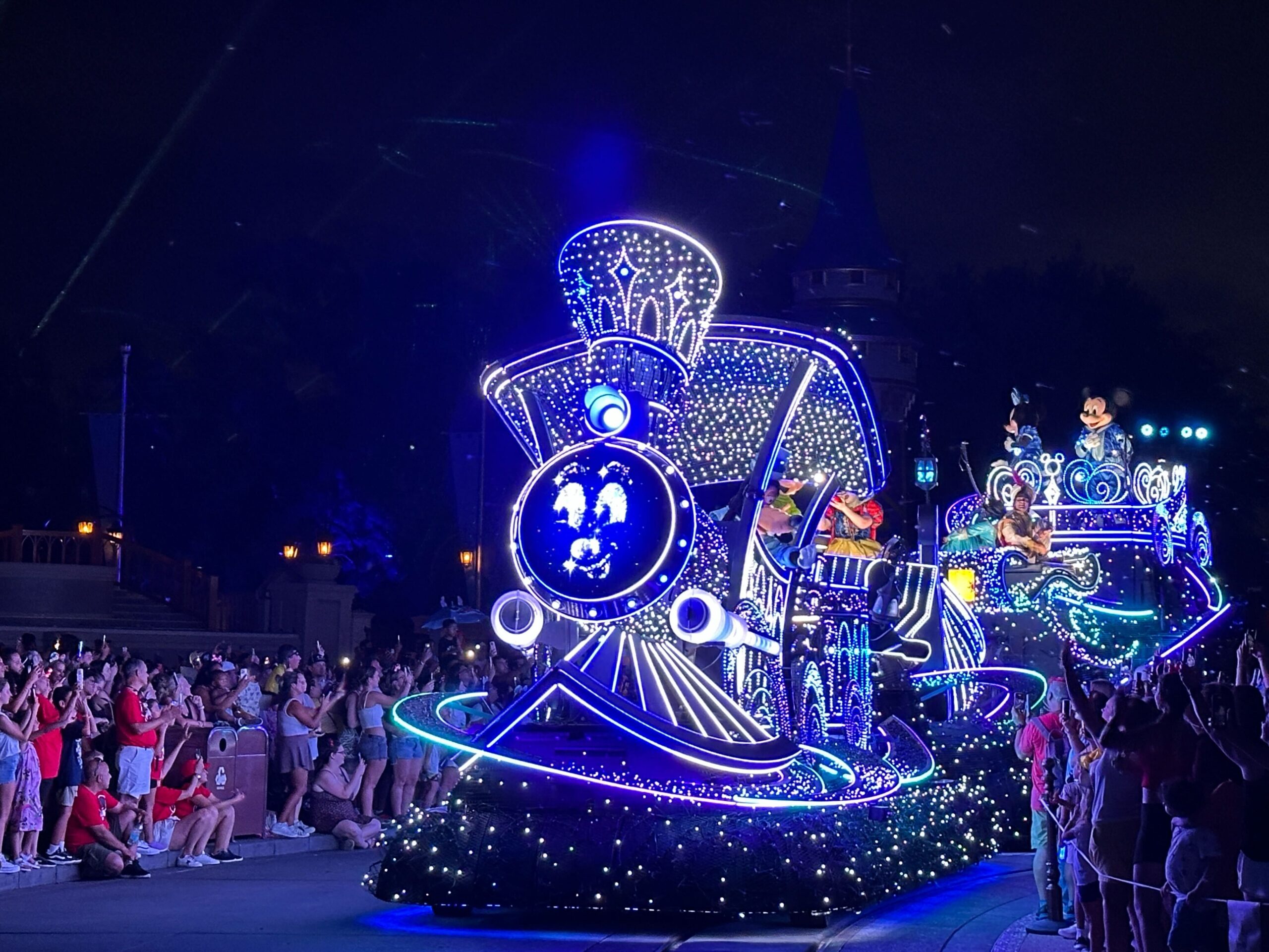 A glowing Disney Starlight Parade float shaped like a train passes cheering crowds—perfect for photos or video.