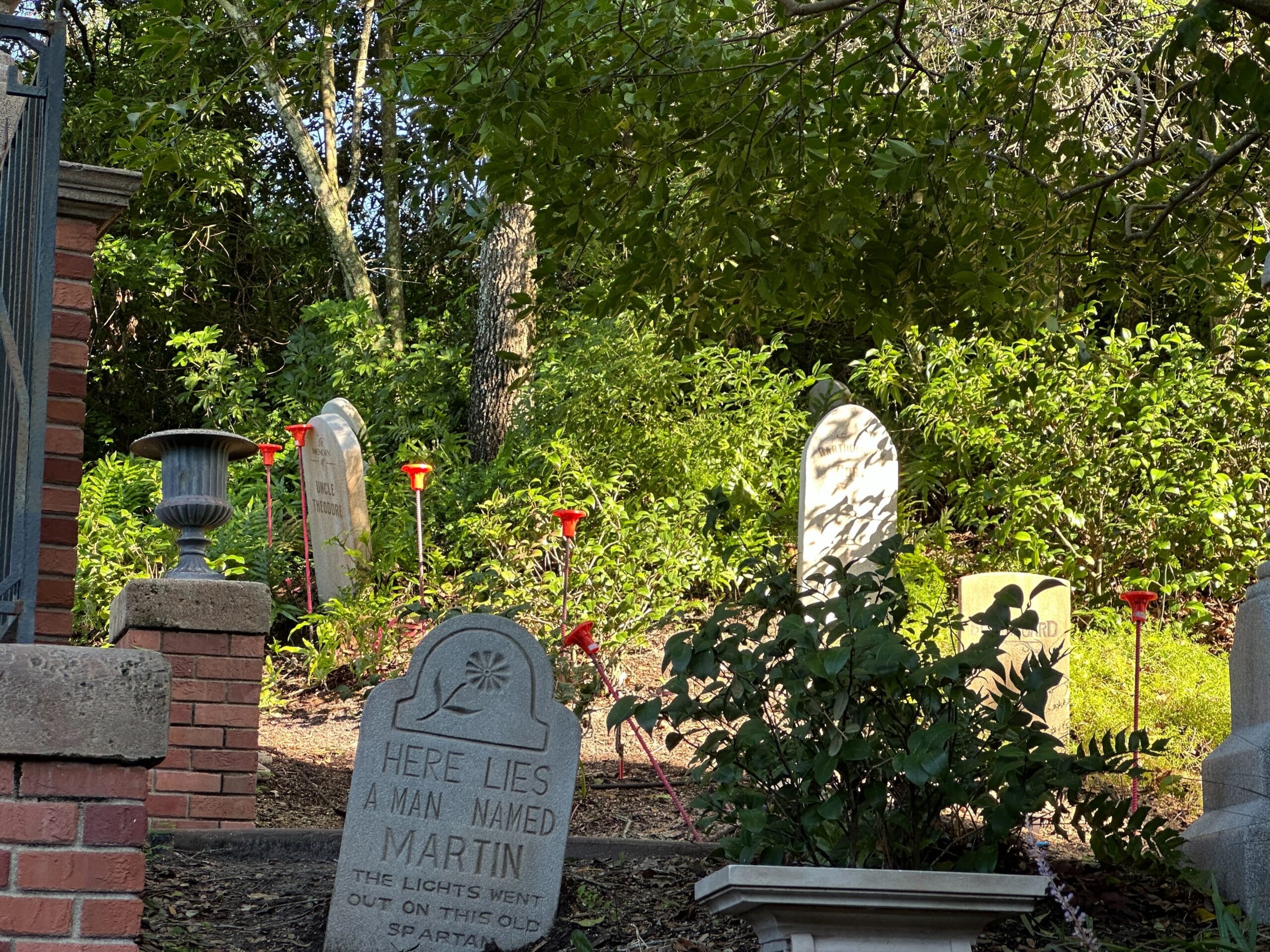 A graveyard scene with headstones and red lanterns, like the Haunted Mansion in Magic Kingdom, sunlight through the trees.