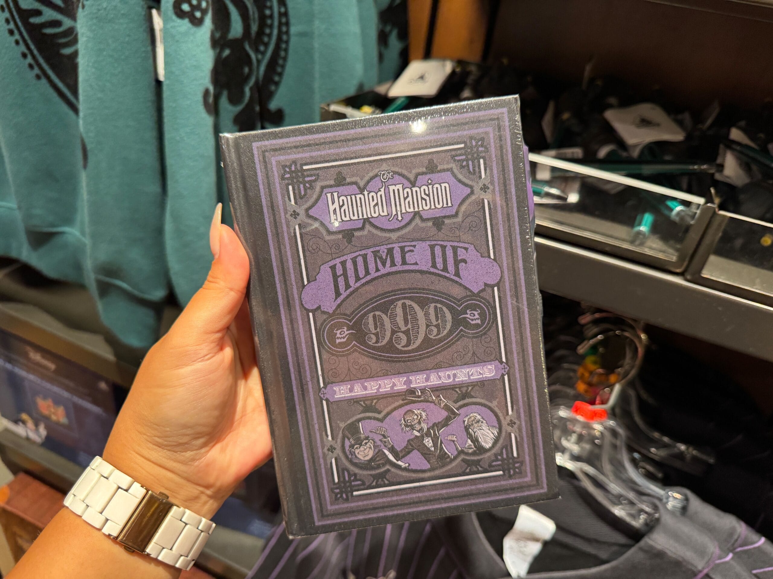 A hand holds a Haunted Mansion journal from the Magic Kingdom merch display.