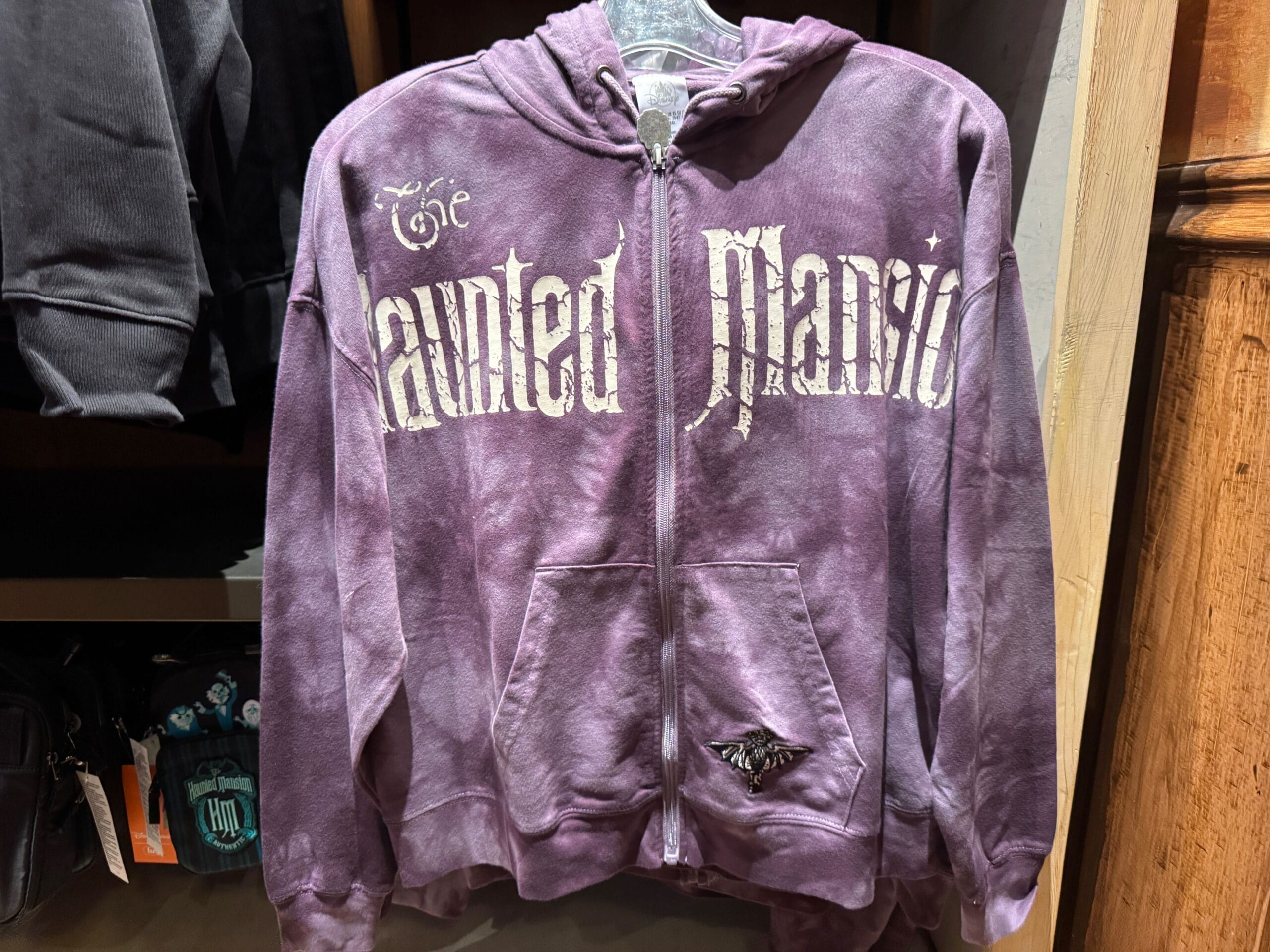 A purple zip-up hoodie featuring Magic Kingdom's Haunted Mansion printed in white gothic letters on the front.