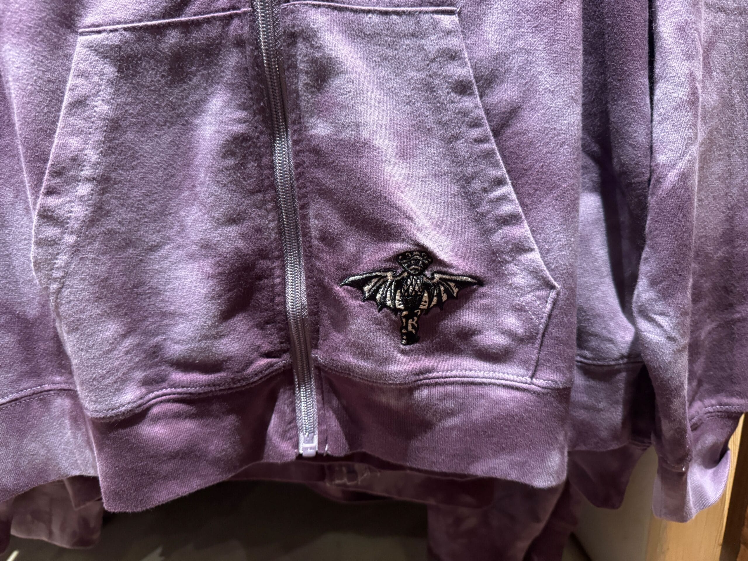 A purple zip-up hoodie with a black embroidered moth patch, inspired by Haunted Mansion merch.