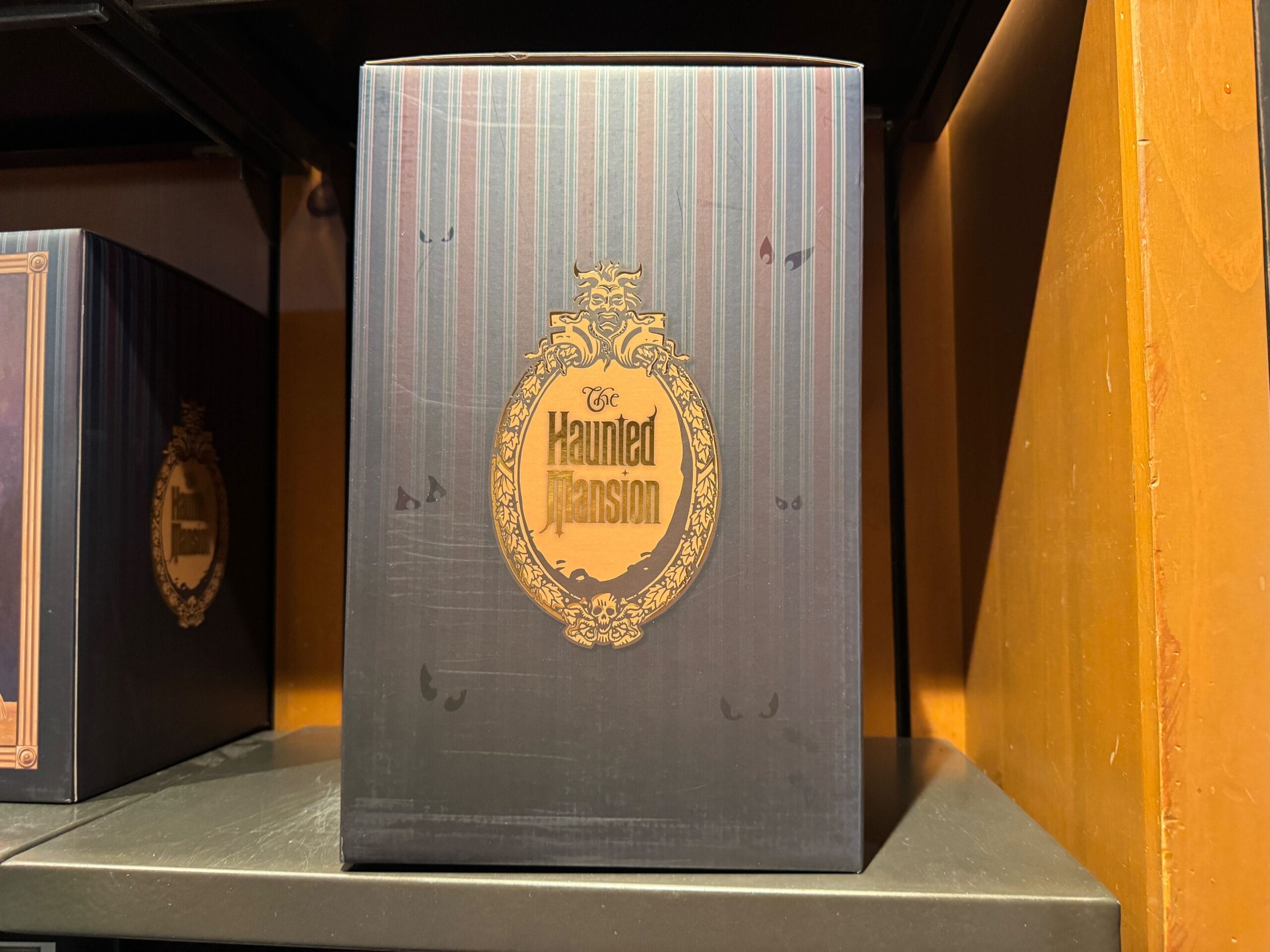 A Haunted Mansion merch box with a gold logo on a dark, striped background, displayed at Magic Kingdom.