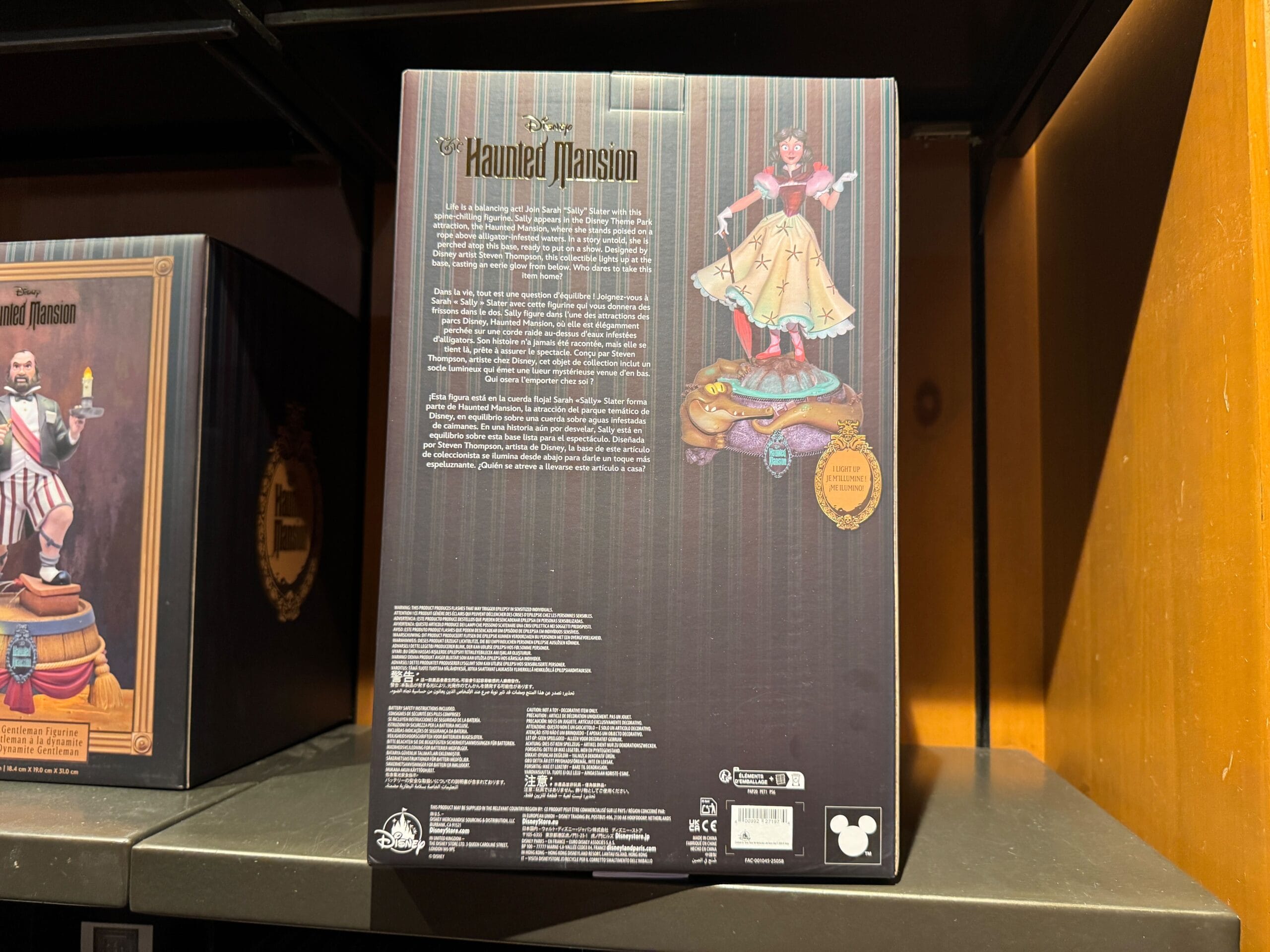 Back of a Haunted Mansion merch box featuring a female figurine in a yellow dress on a tightrope. Magic Kingdom icon.