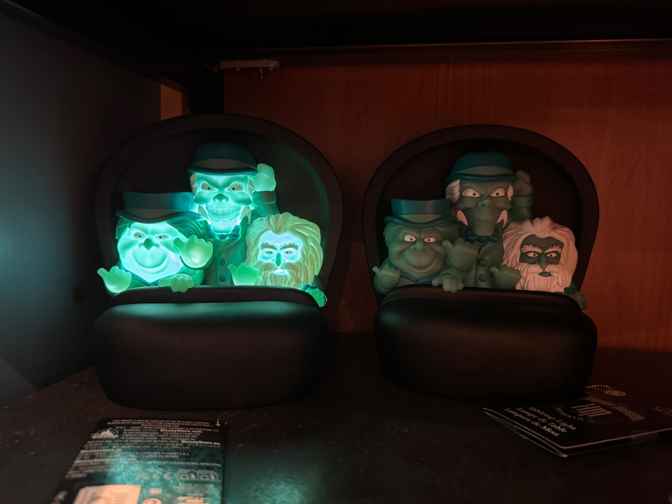 Two Haunted Mansion merch figurines—ghosts in black ride vehicles—glow eerily, straight from Magic Kingdom shelves.