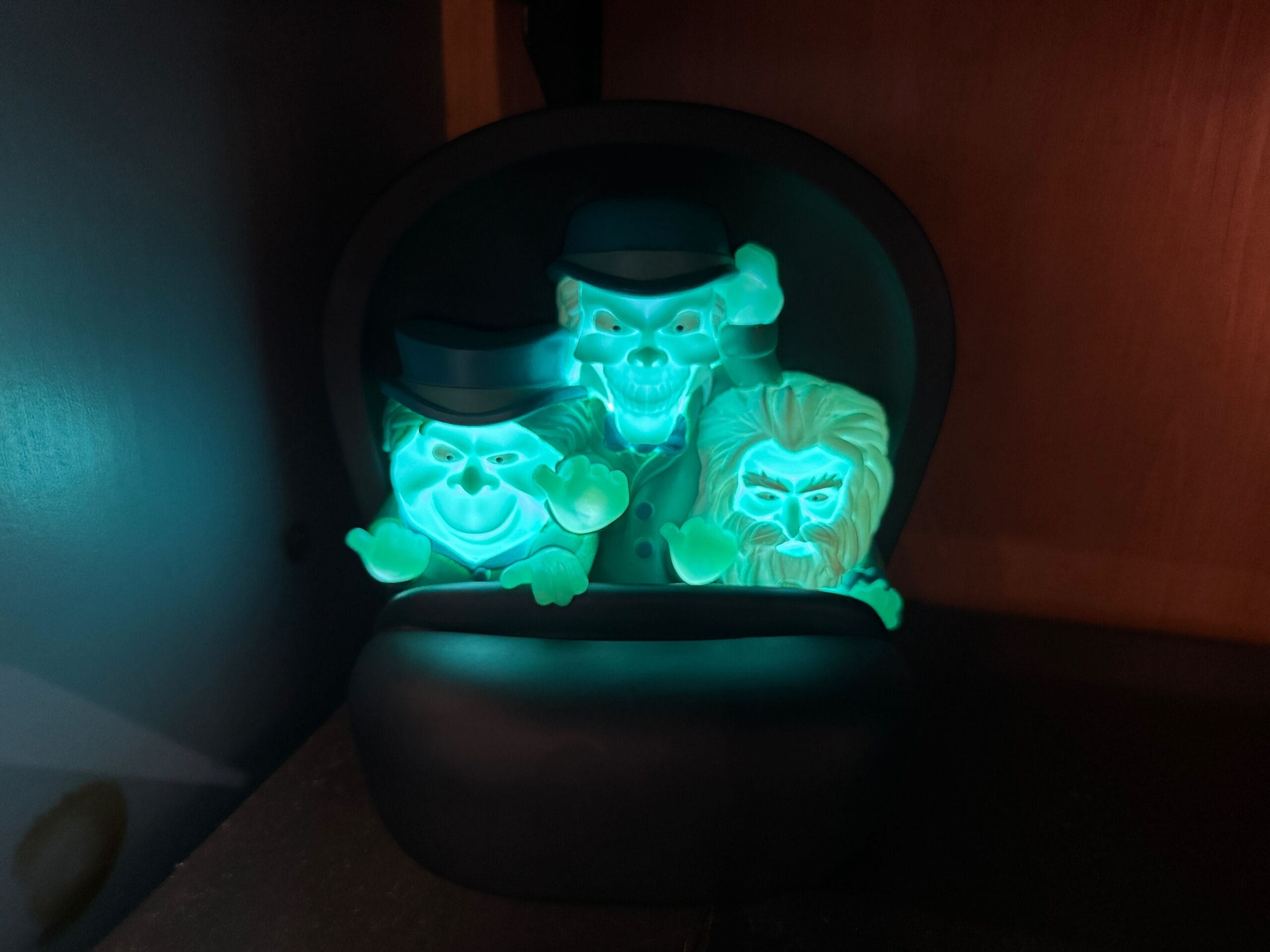 Three ghostly figures with glowing faces sit together inside a Haunted Mansion container on a shelf.