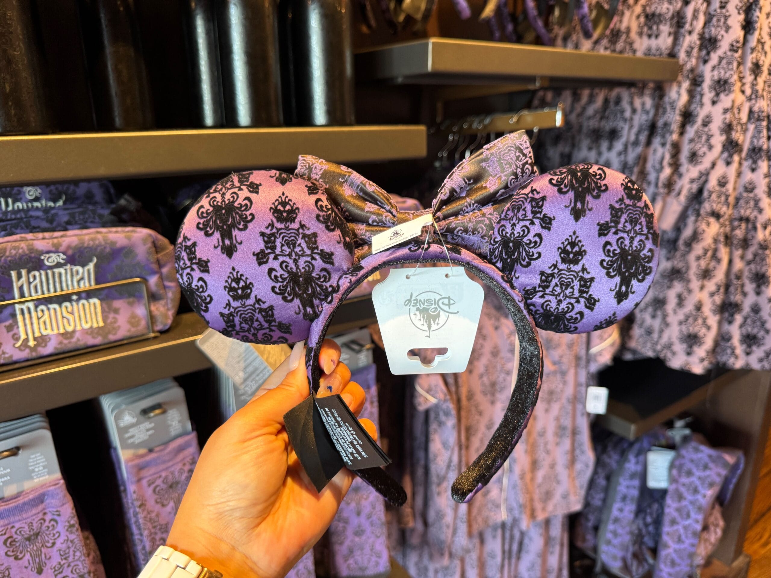 Hand holding purple and black Haunted Mansion Minnie Mouse ears headband in Magic Kingdom merch store.