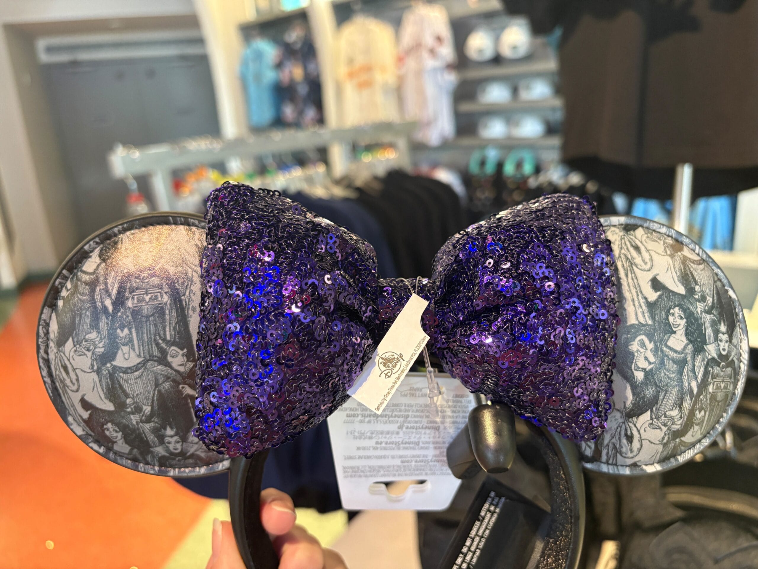 Disney Villains Ears headband with black-and-white print and a large purple sequin bow displayed in store.