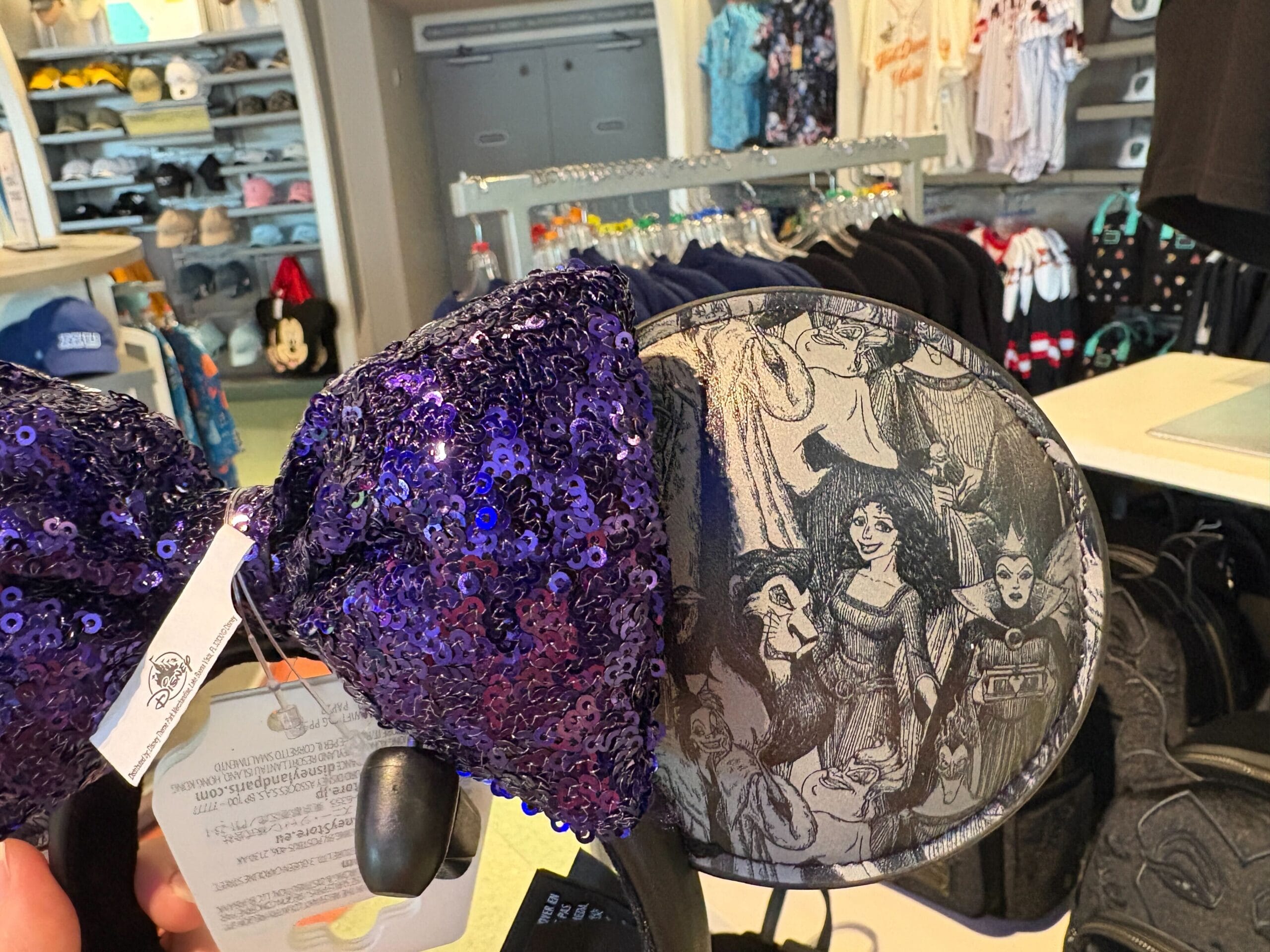 A sequined purple Disney headband with Maleficent Villains artwork on the ears displayed in a merchandise store.