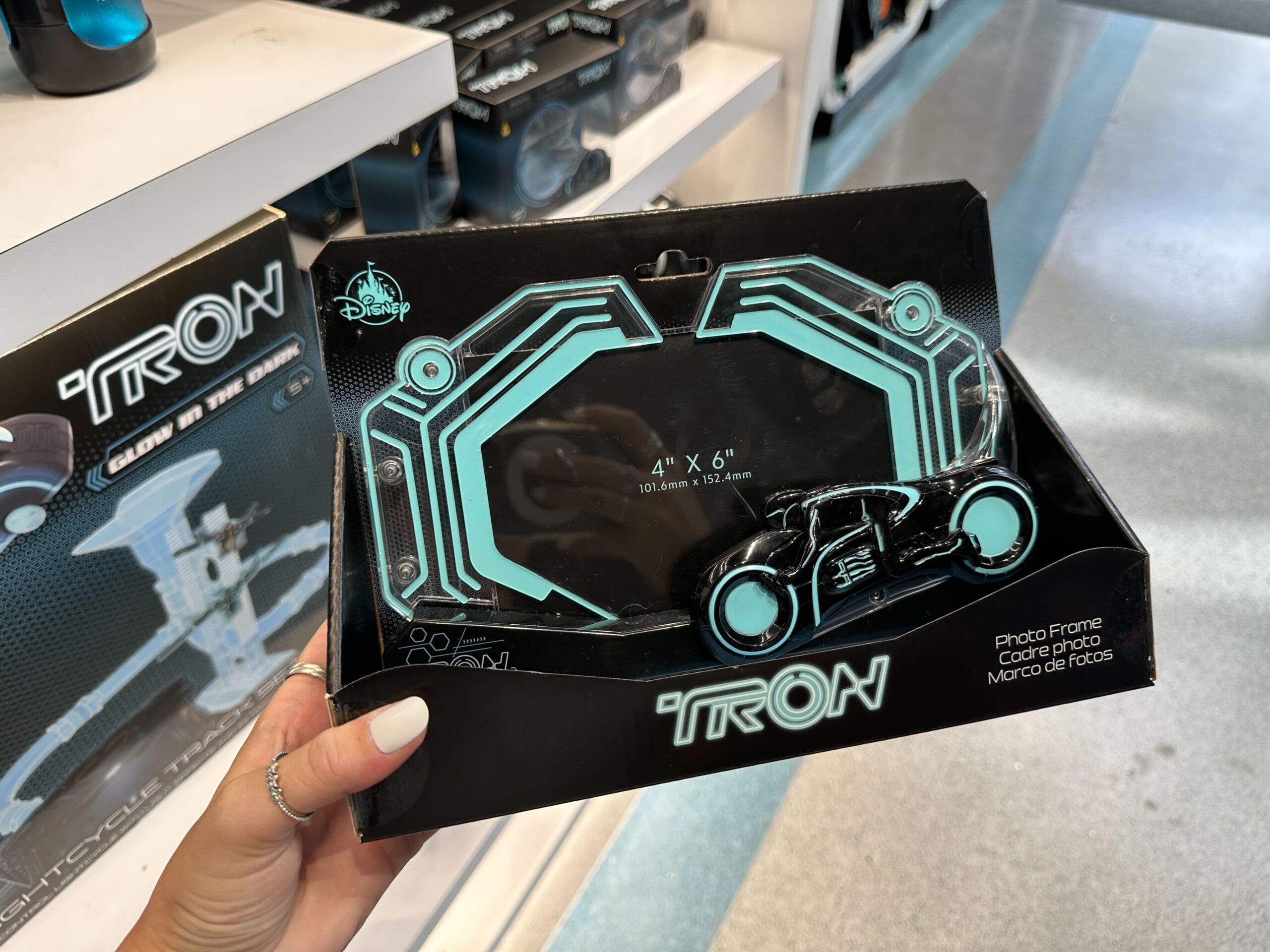 A hand holds a TRON-themed photo frame shaped like a lightcycle, displayed in a store.