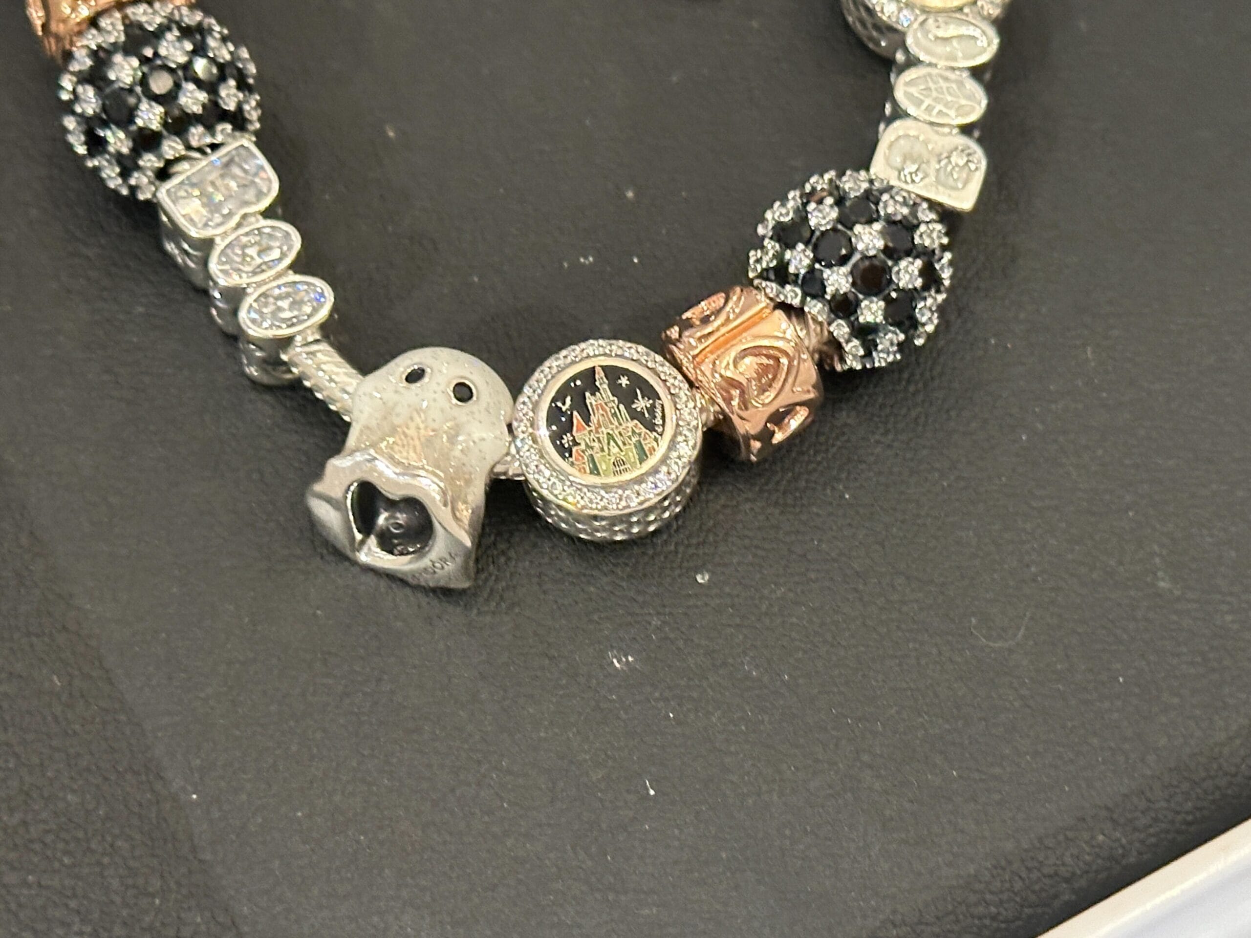 A charm bracelet featuring a castle charm, a ghost charm, black and silver bead charms, and rose gold accents on a black surface.