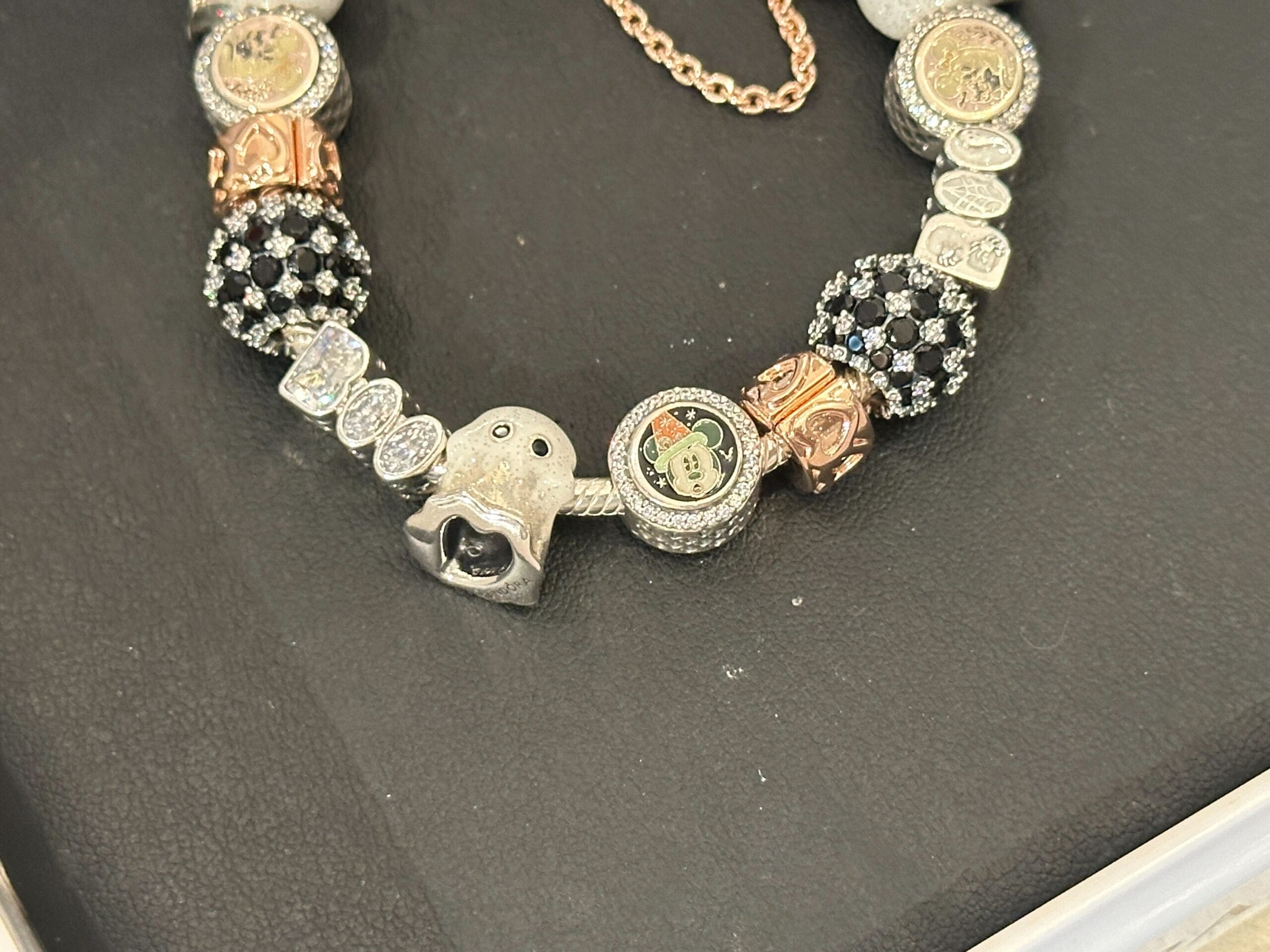 A charm bracelet with various silver, gold, and jeweled beads on a black surface.