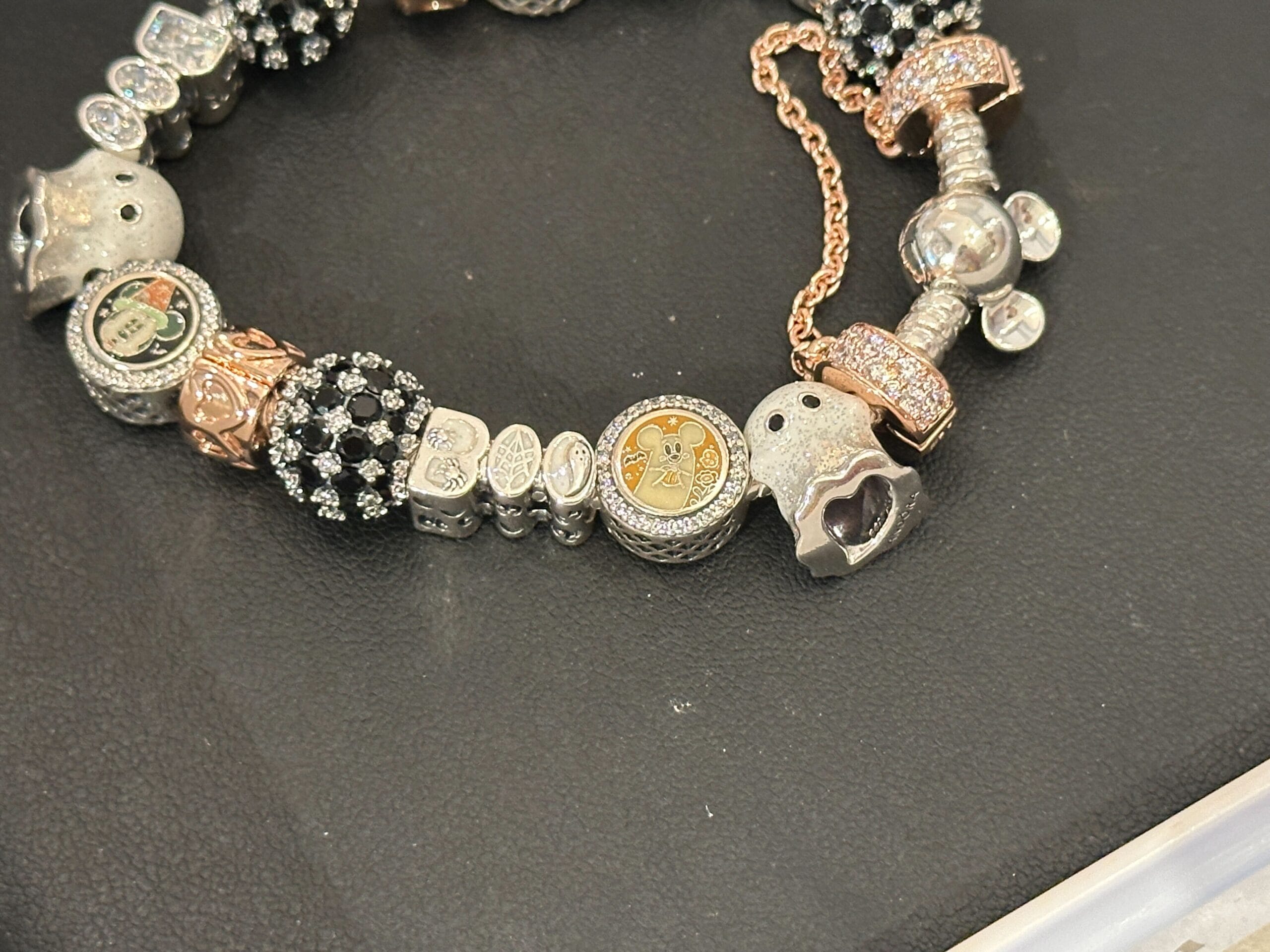 A close-up of a charm bracelet with various silver and gold charms on a black textured surface.