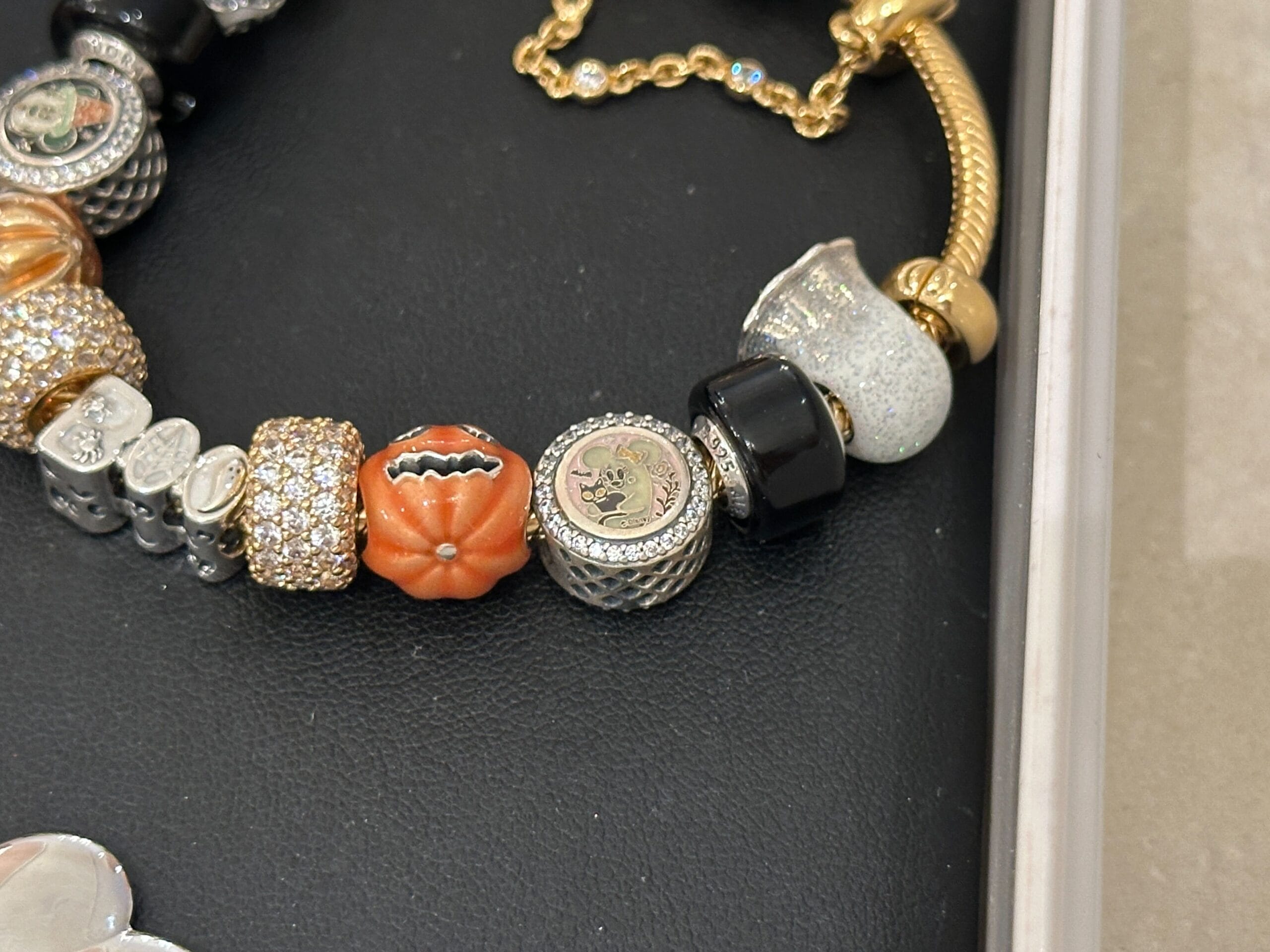 A charm bracelet with Pandora Charms, featuring a pumpkin, bat, and sparkling gold and silver charms on a black surface.