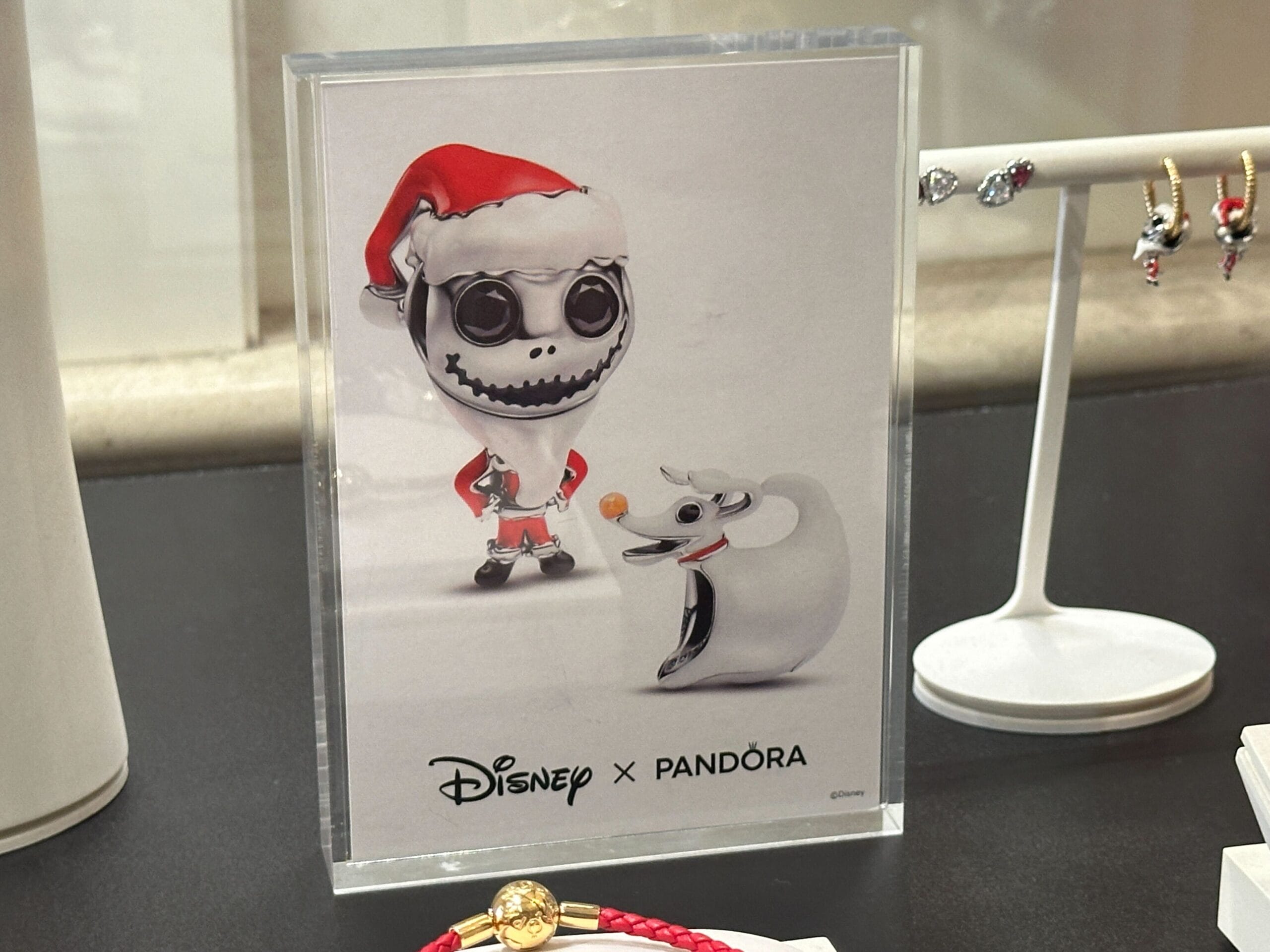 Display sign featuring Disney x Pandora with Jack Skellington in a Santa suit and ghost dog Zero, next to jewelry.