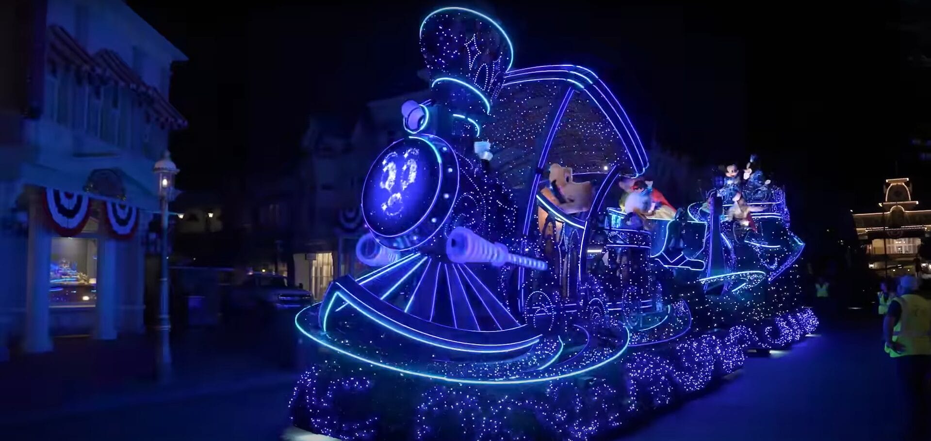 A brightly lit parade float shaped like a train, glowing with blue lights, brings Disney Starlight magic to the night street.