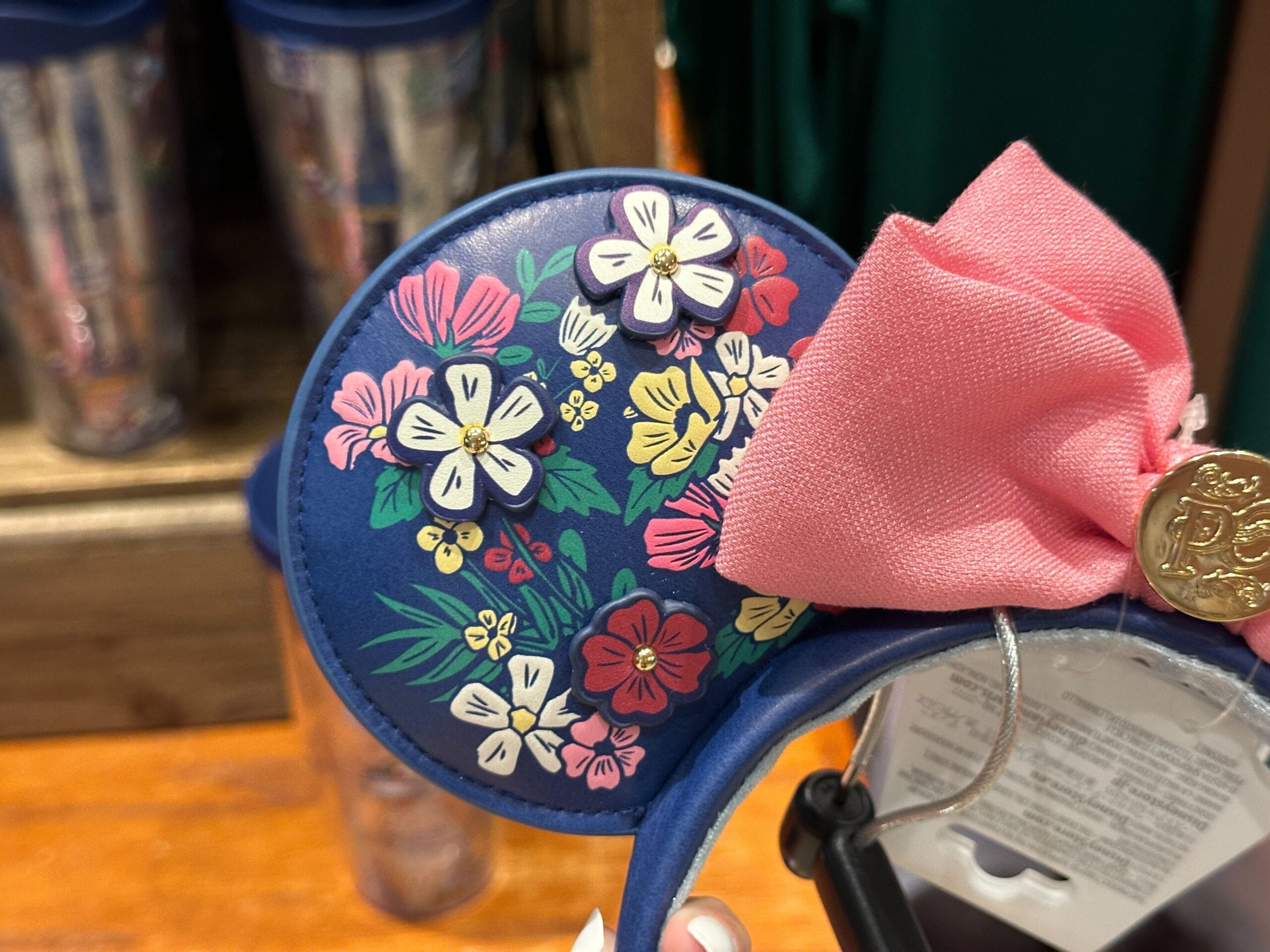 Blue Mickey ear headband with colorful floral designs and a large pink bow on one ear, displayed in a store.