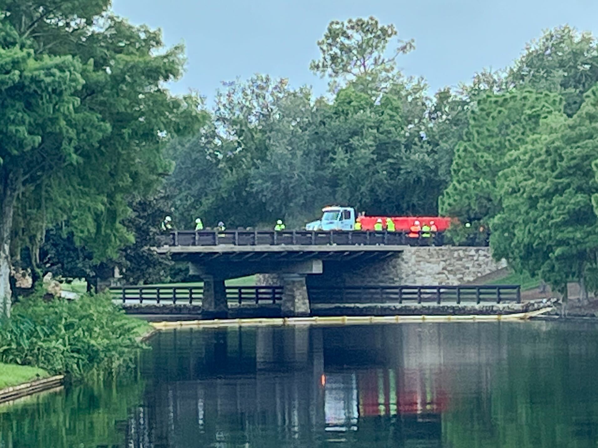 A group of workers and a truck are on a wooden bridge over a calm river at Disney's Port Orleans Resort.