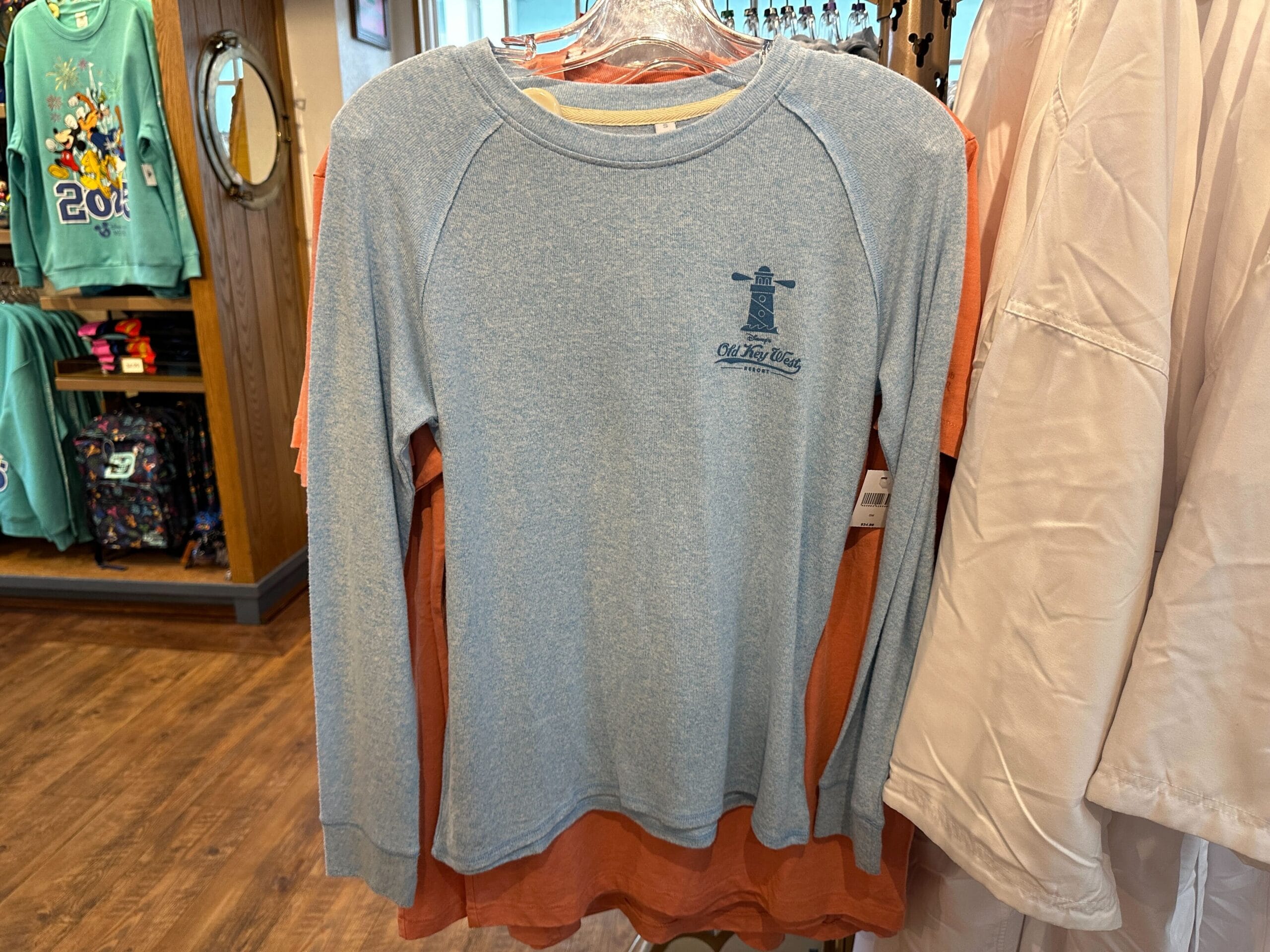 A group of Disney Vacation Club Apparel shirts, including an Old Key West T-Shirt, displayed on a swinger.