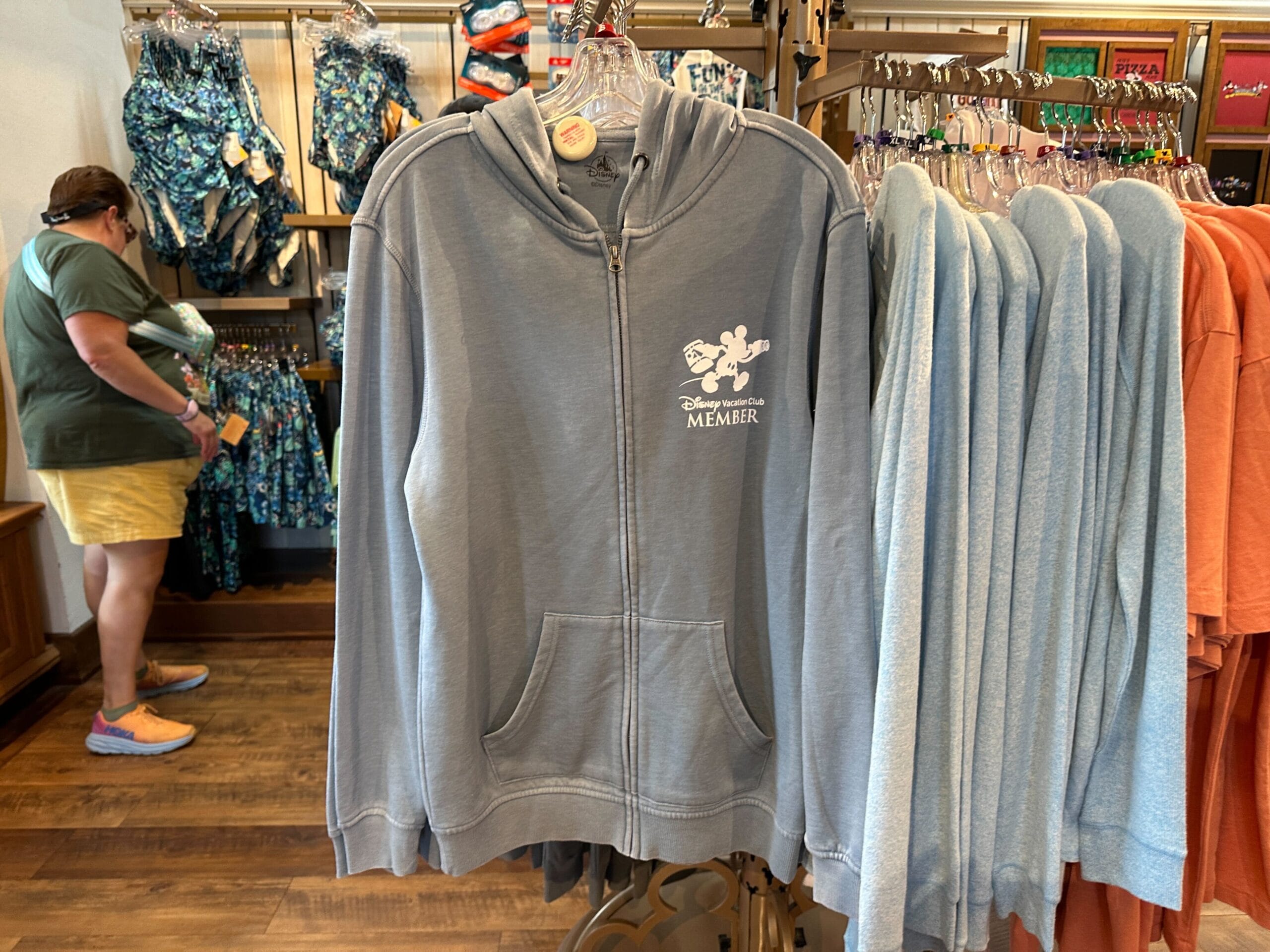 Gray zip-up hoodie with Mickey Mouse and Disney Vacation Club Member text, seen in a retail store near the Old Key West T-Shirt.