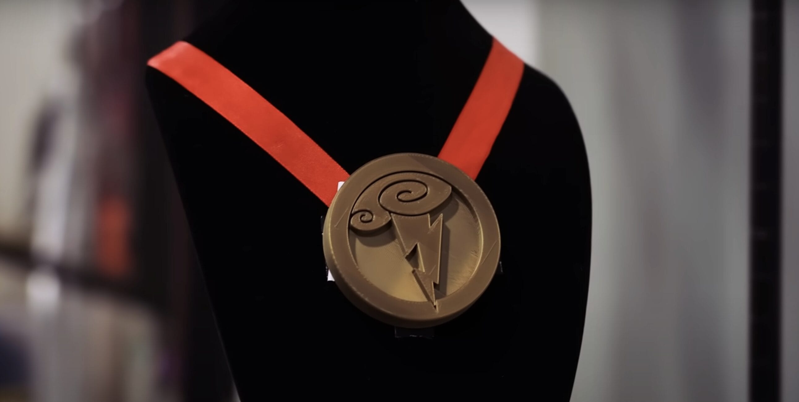 A round, bronze medal with a red ribbon, inspired by Hercules Stage Show's "Zero to Hero," on a black mannequin bust.