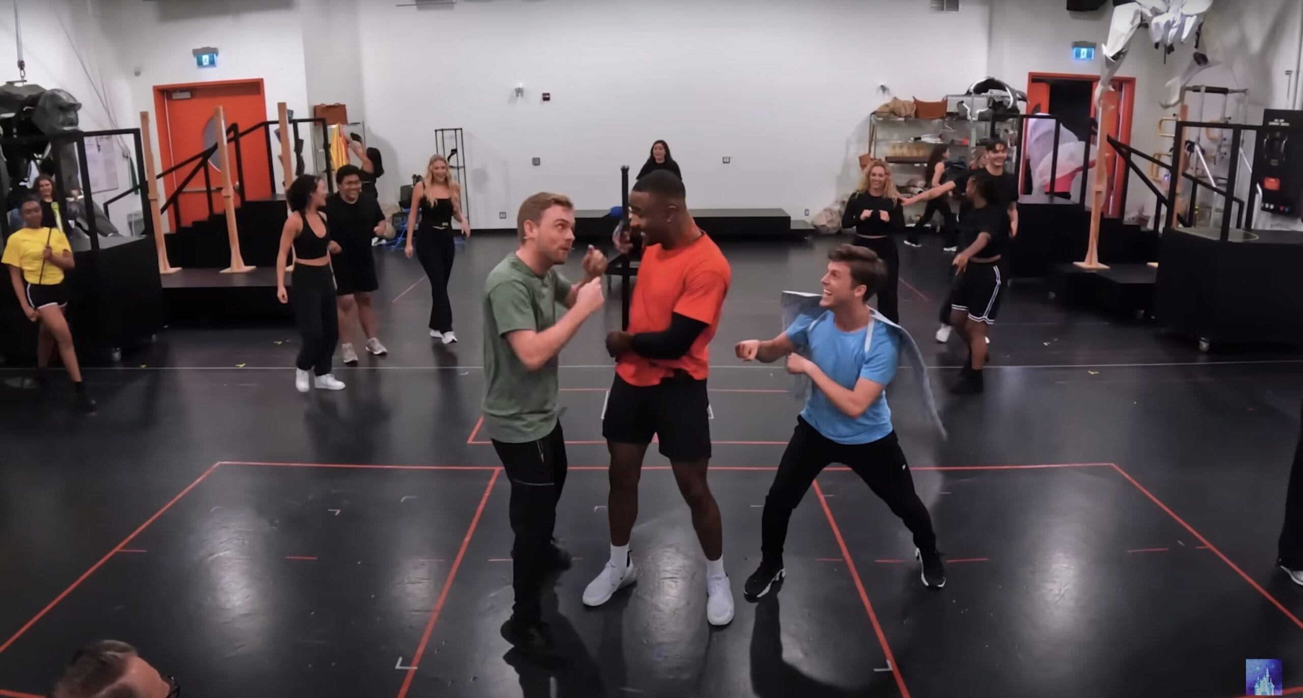 Three men sing and gesture dramatically in a Disney Cruise Line Hercules Stage Show rehearsal, dancers moving behind them.