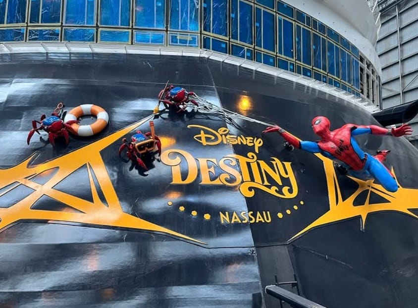 Four Spider-Man figures, the Stern Characters on Disney Destiny, scale the cruise ship near its logo and giant windowed deck.