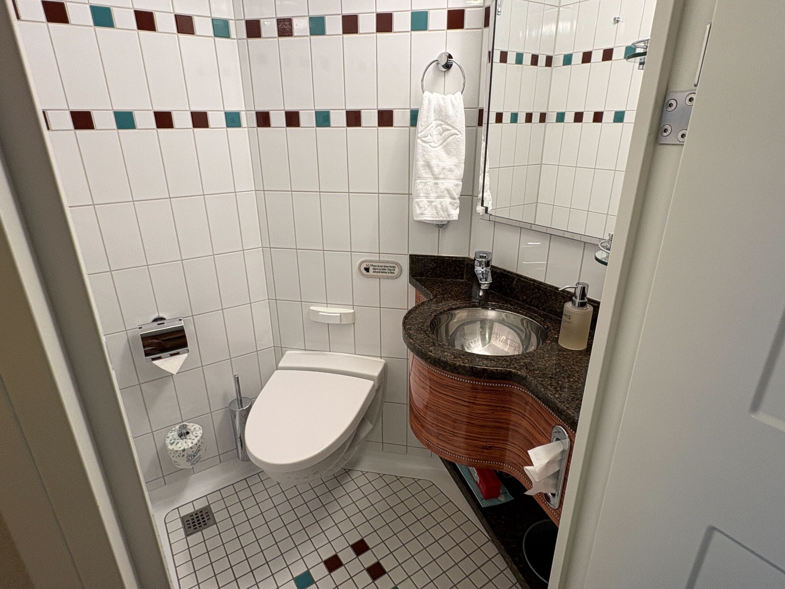 Small bathroom in a Concierge Family Oceanview Stateroom with tiled walls, corner sink, and mirror on a Disney Dream cruise ship.