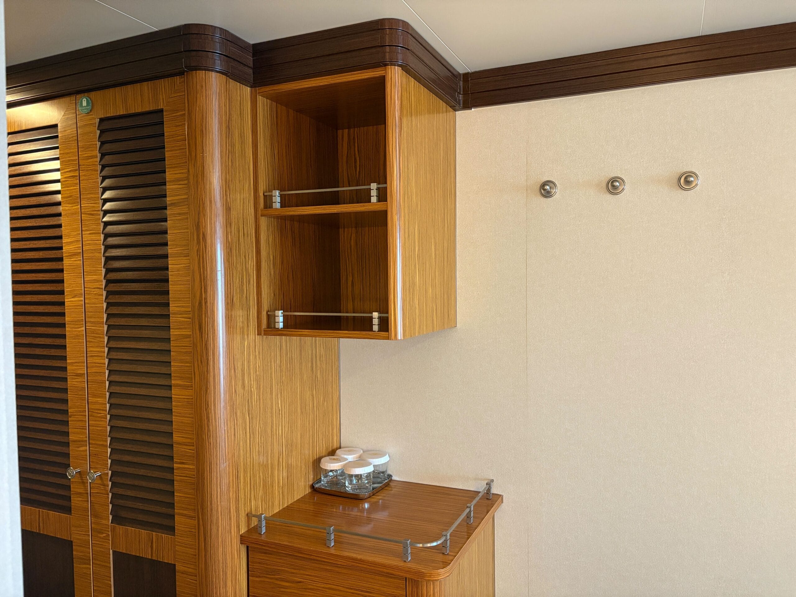 Wooden cabinets, open shelves, and stacked cups create a modern vibe in a Disney Dream Concierge Family Oceanview Stateroom.
