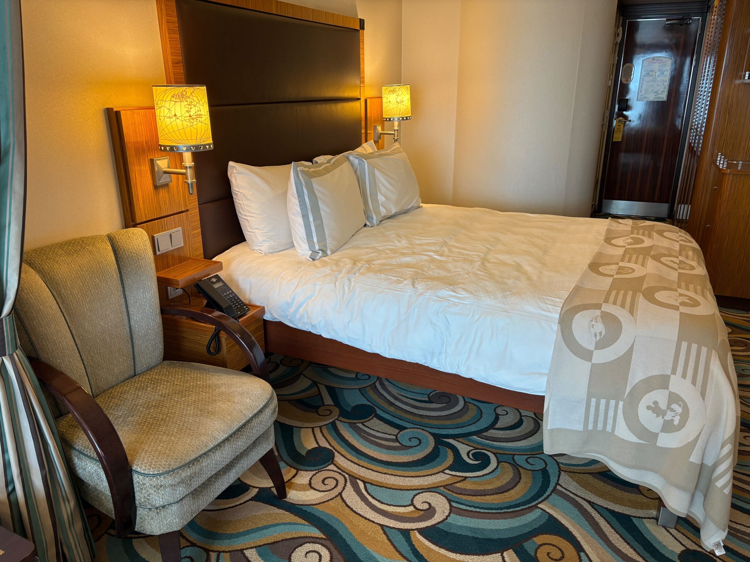 A neatly made bed with white linens and a beige blanket in a Concierge Family Oceanview Stateroom on Disney Dream Cruise Ship.