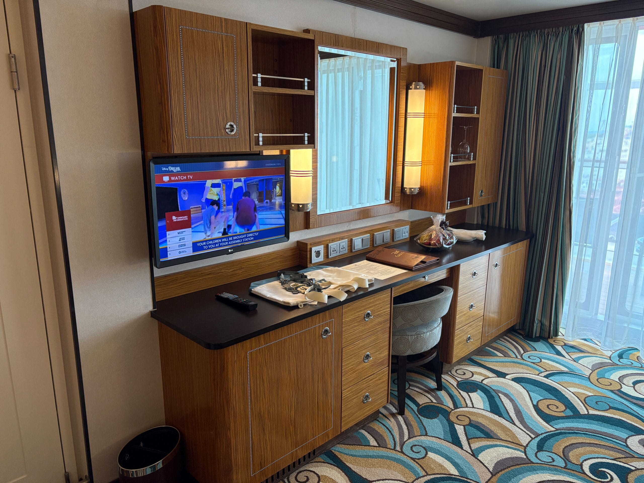 Wooden desk with TV, mirror, chair, and carpet; food tray atop—found in a Disney Dream Concierge Family Oceanview Stateroom.