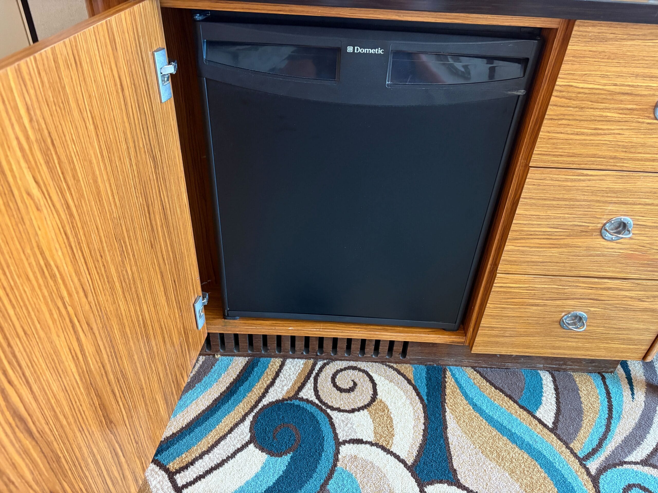 A small black refrigerator in a wooden cabinet, door open, in a Concierge Family Oceanview Stateroom.