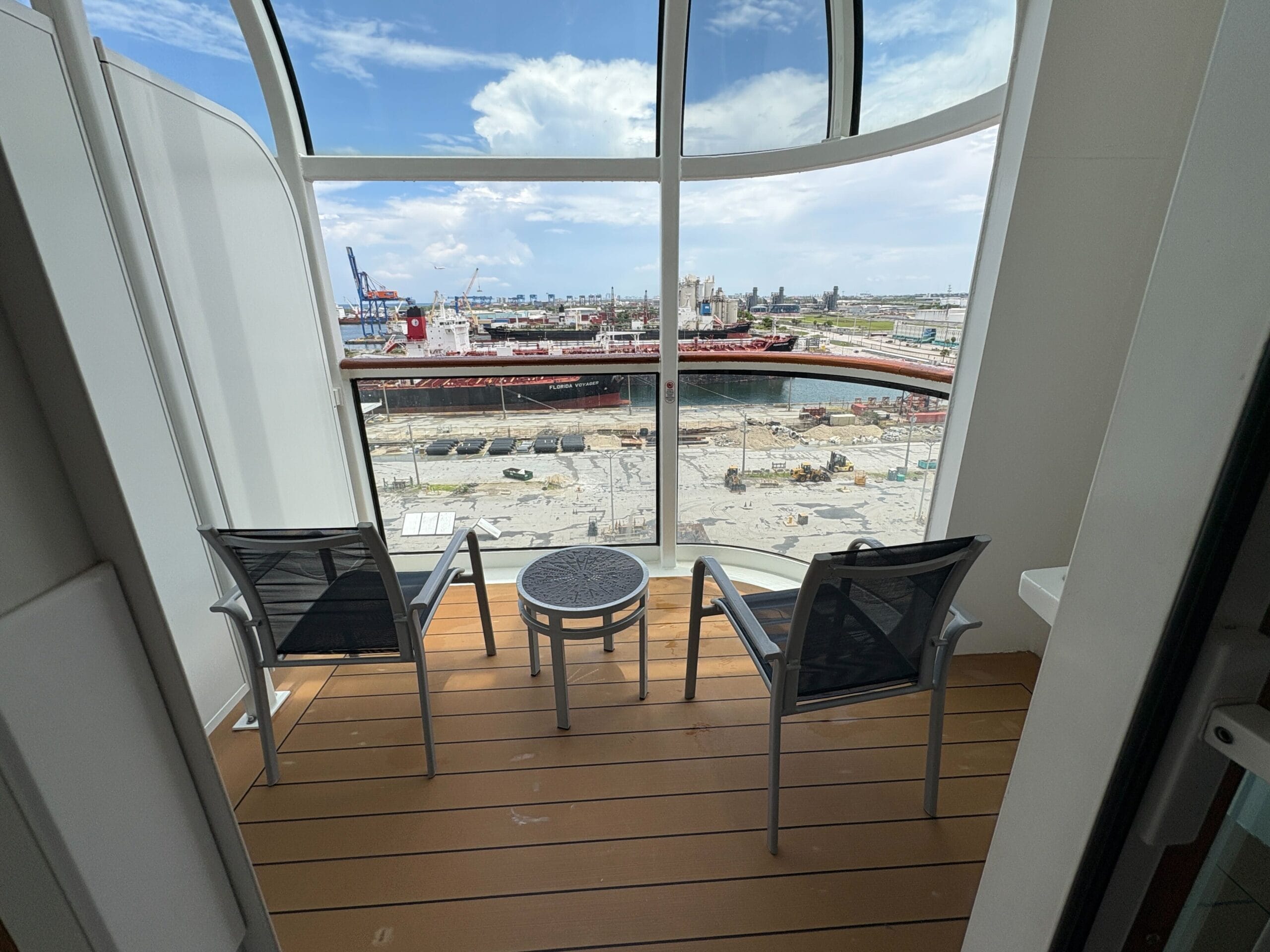 Two chairs and a table on the verandah overlook the port, with ships and the Disney Dream Cruise Ship in view.