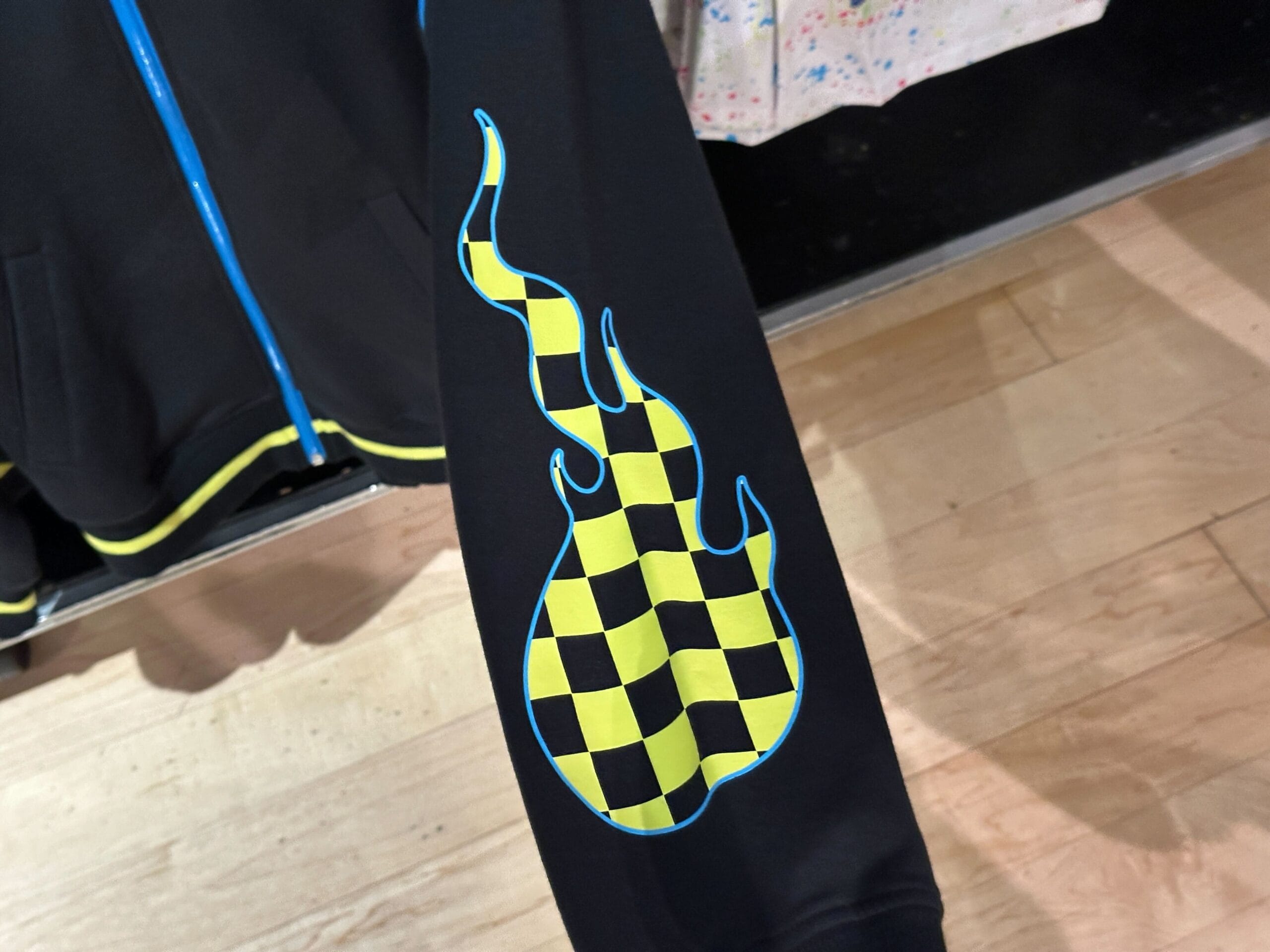 Black apparel sleeve featuring a yellow and black checkered flame graphic, inspired by Rock 'n' Roller Coaster.