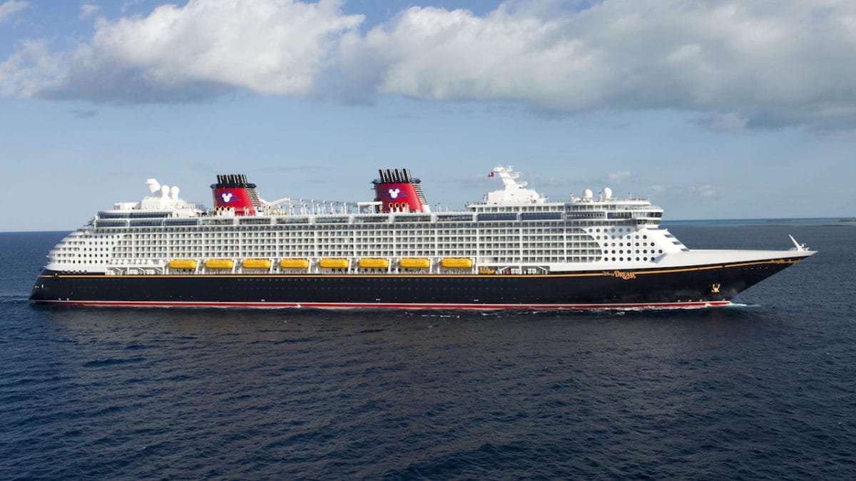 A Disney Cruise Line ship with red funnels sails on a calm blue sea under a partly cloudy sky for breaking news about Disney Cruise ship overboard incident.