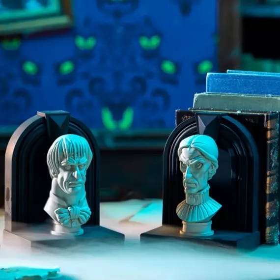 Two stern-looking bust bookends sit on a table with spooky, glowing green eyes in the blurry background.
