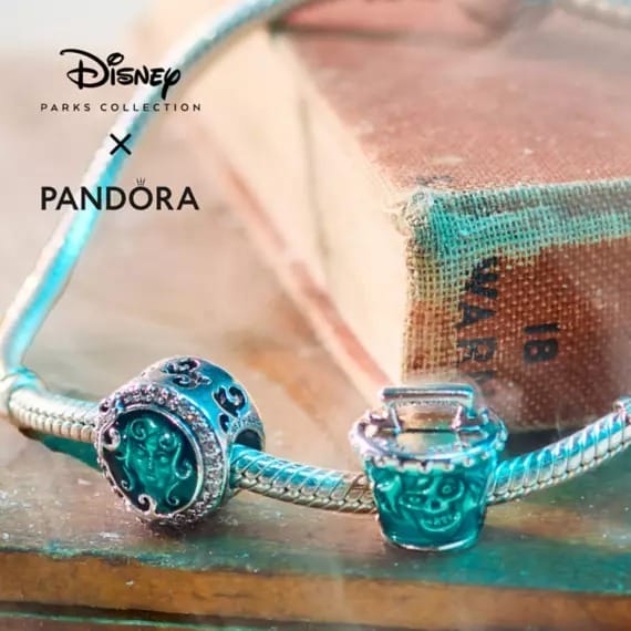 A Disney x Pandora silver bracelet with teal Haunted Mansion-themed charms is displayed on an old book.