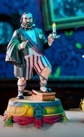 A Haunted Mansion figurine of a man in a suit jacket and shorts holds a candlestick atop a decorated pedestal.