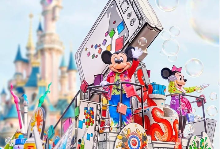Mickey and Minnie Mouse wave on a Colour Parade float at Disneyland Paris, bubbles floating near the castle in 2026.