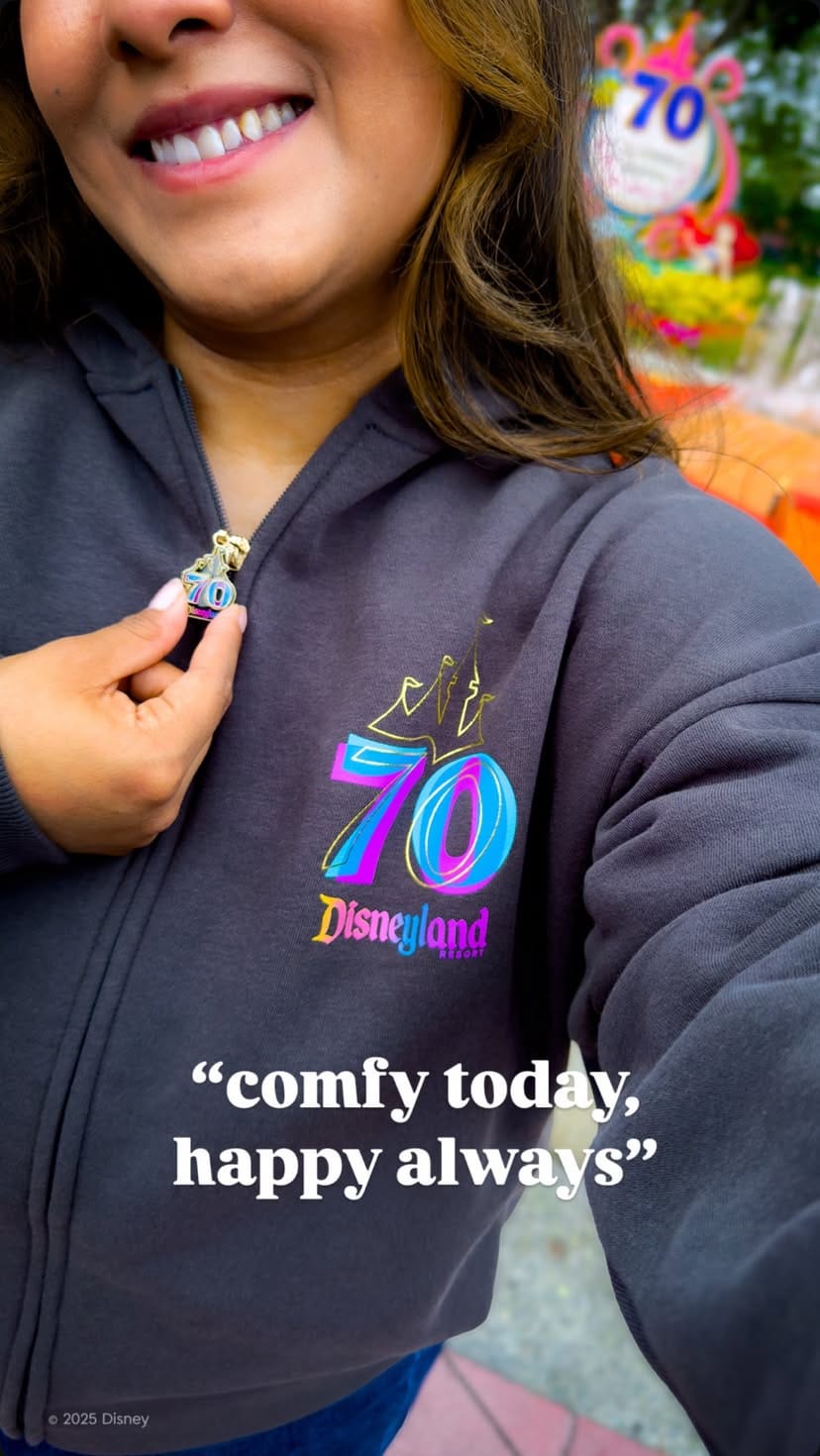 A woman smiles in a Disneyland 70th Anniversary hoodie, holding the zipper; text reads "comfy today, happy always.