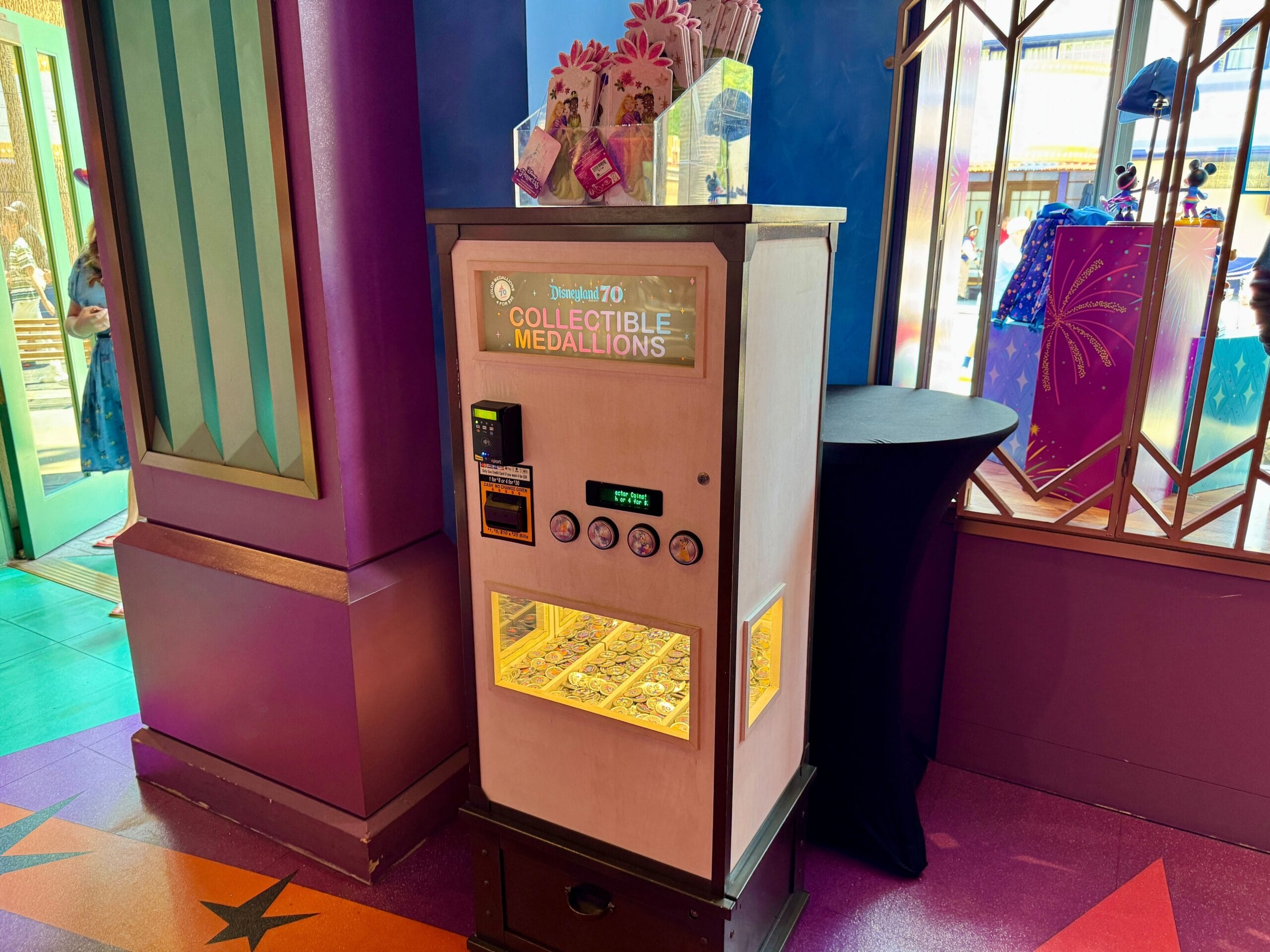 A vending machine for collectible medallions stands indoors near Disneyland 70th Anniversary-themed Disney decor.