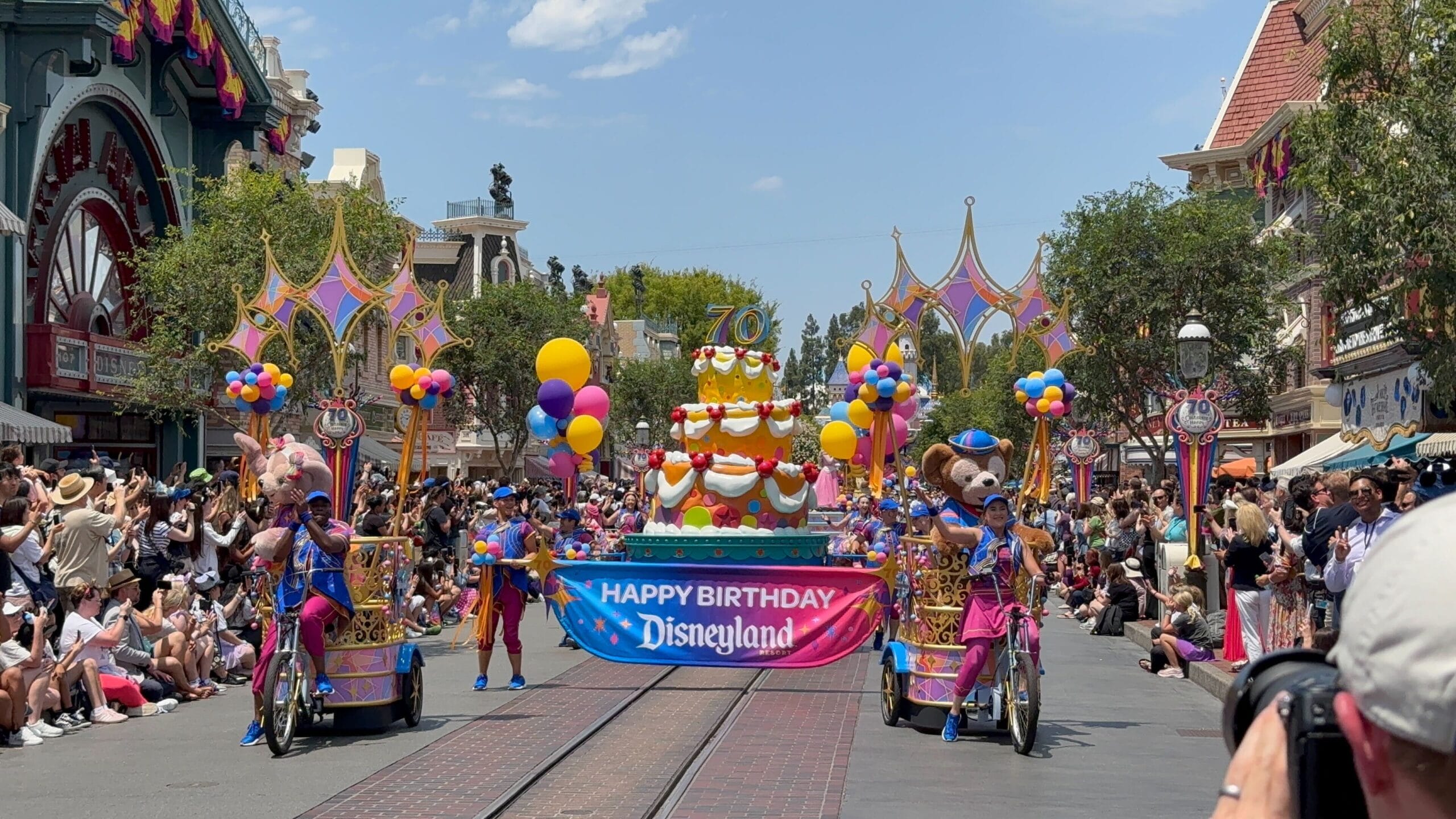 Disneyland birthday cavalcade with a giant cake float, performers, and a "Happy Birthday Disneyland" banner on Main Street.