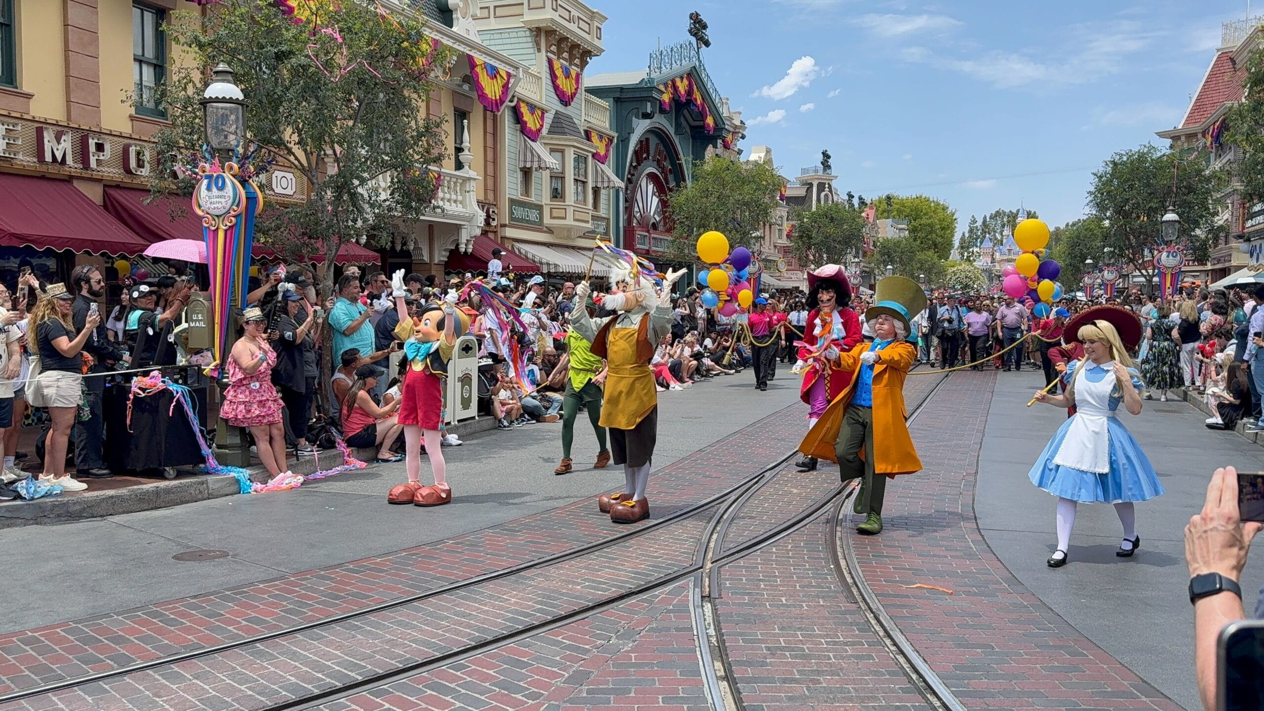 Disneyland birthday cavalcade features Disney characters parading down the street, delighting the sunny-day crowd.