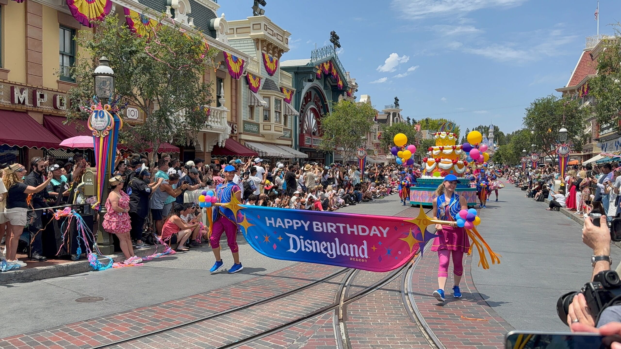 Two performers hold a "Happy Birthday Disneyland" banner during the lively Disneyland birthday cavalcade on Main Street.