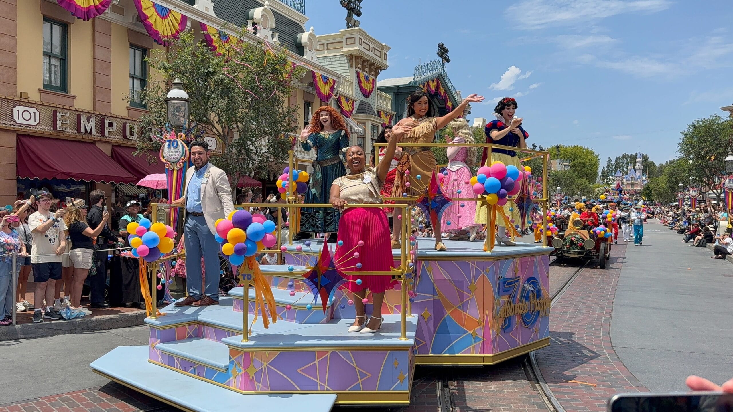 Colorful Disneyland Birthday Cavalcade float with Disney princesses waving to crowds on a sunny, decorated street.