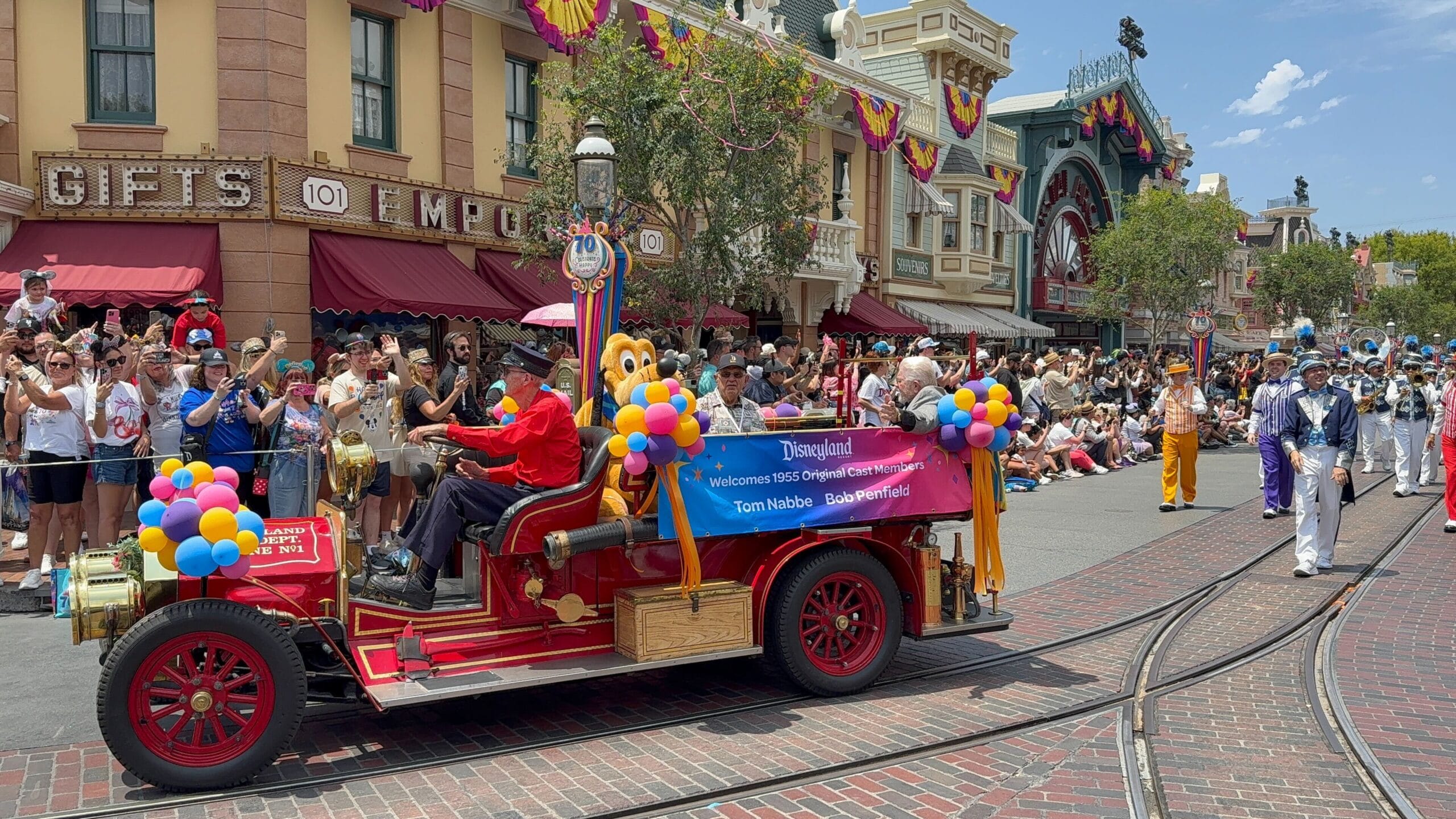 Colorful parade float with Pluto and people in fire truck celebrate a Disneyland birthday cavalcade on festive Main Street.