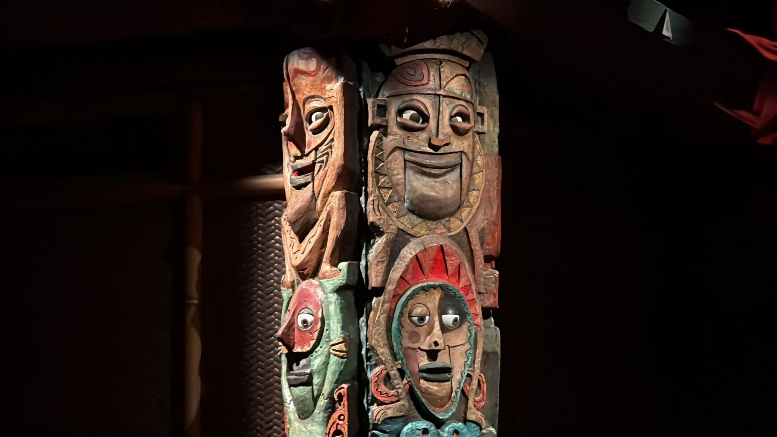 A carved wooden totem pole with colorful, expressive faces lit against a dark background.
